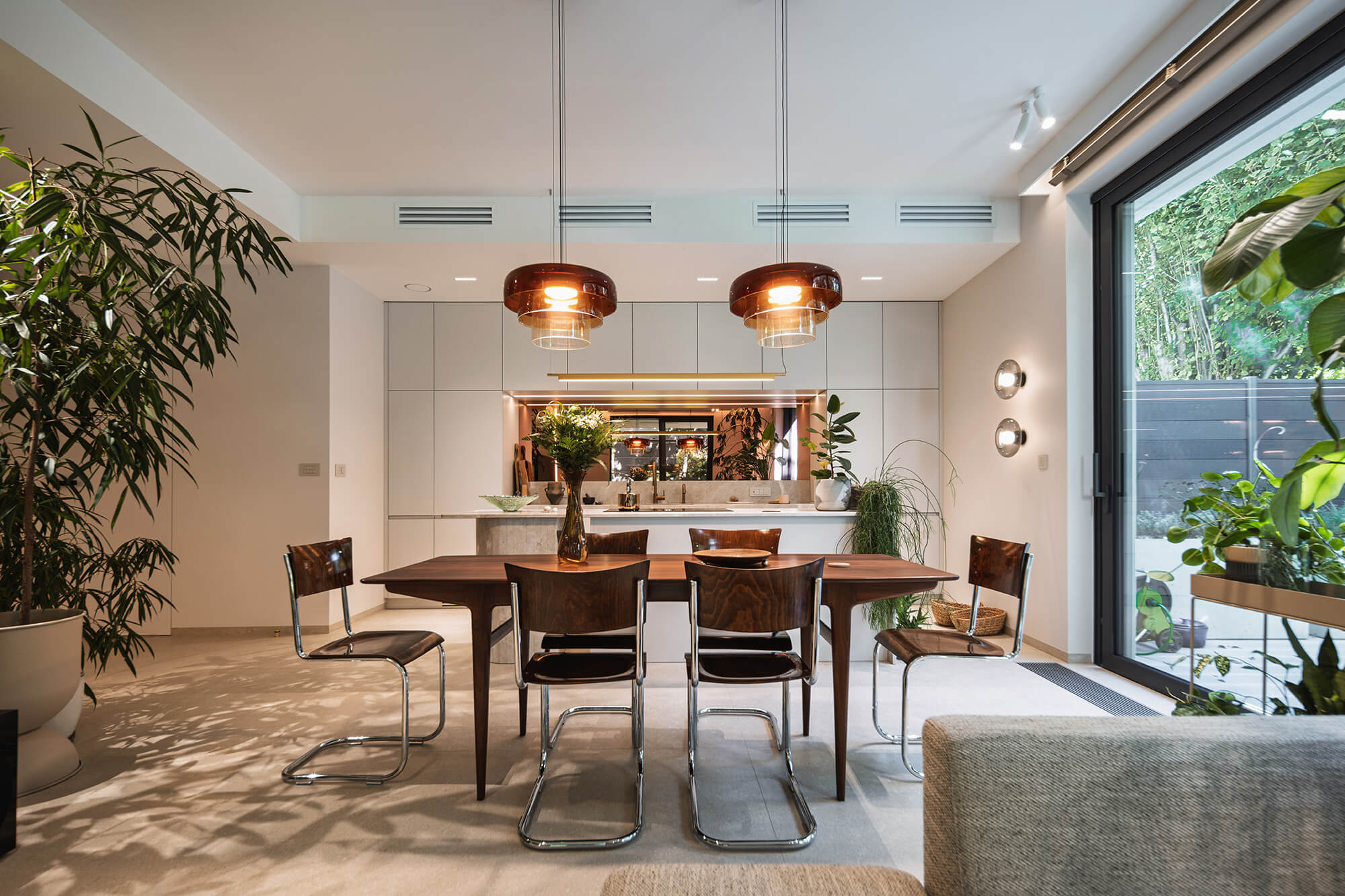 Nowoczesna jadalnia z drewnianym stołem, krzesłami i roślinami doniczkowymi.