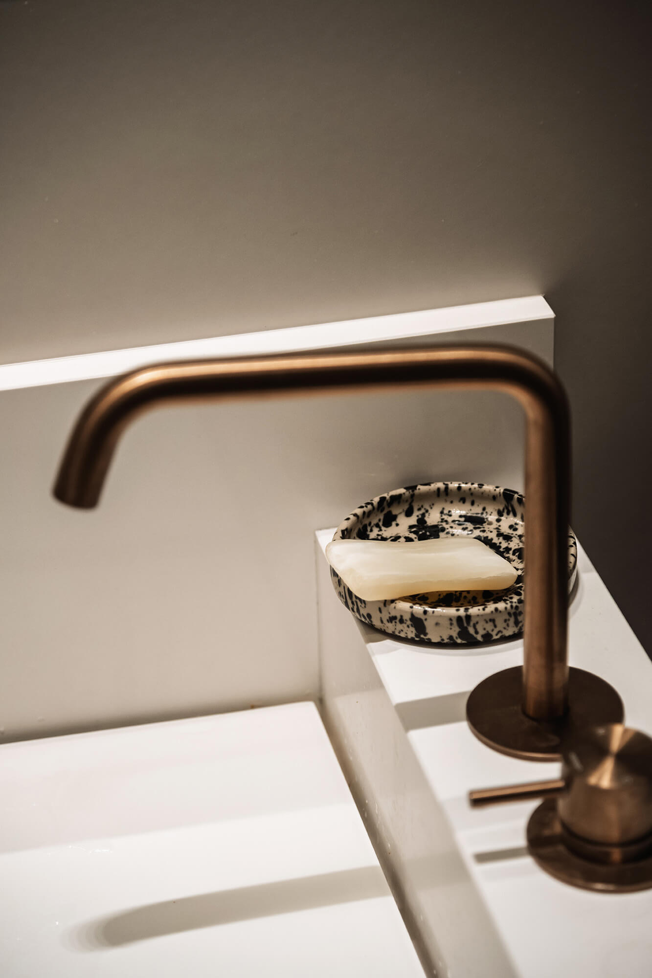 Złoty kran nad białą umywalką z mydłem w designerskiej mydelniczce.
