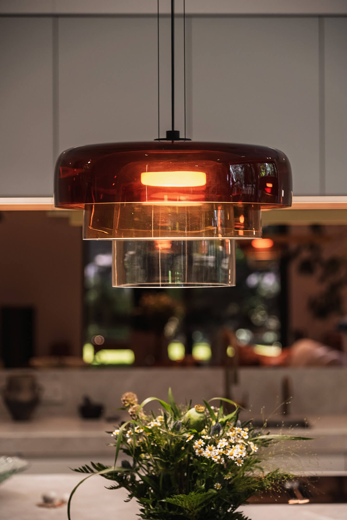 Stylowa, warstwowa lampa wisząca w odcieniach brązu nad kwiatami.