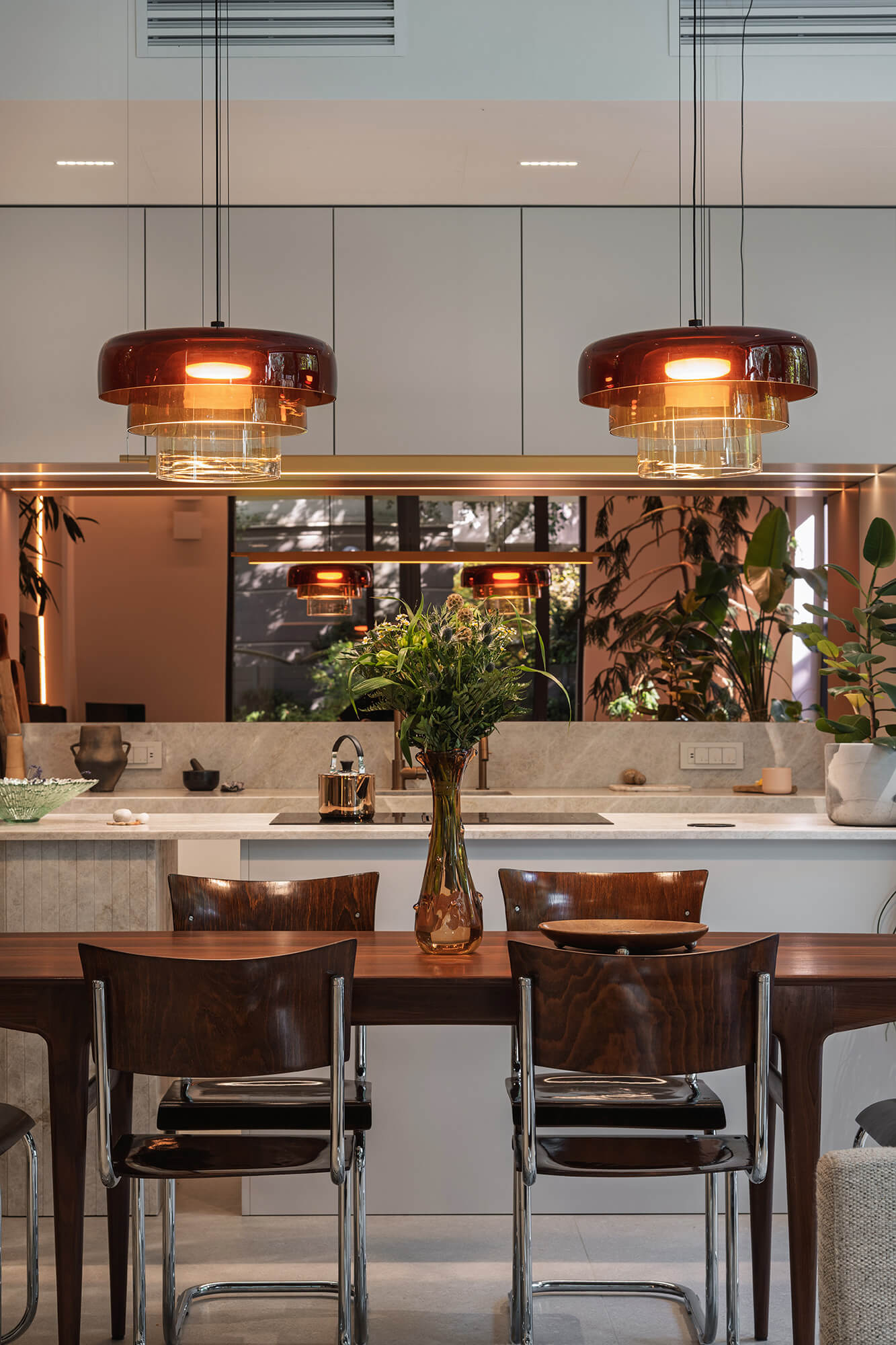 Minimalist modern kitchen with wood table, chairs, and amber pendant lights.