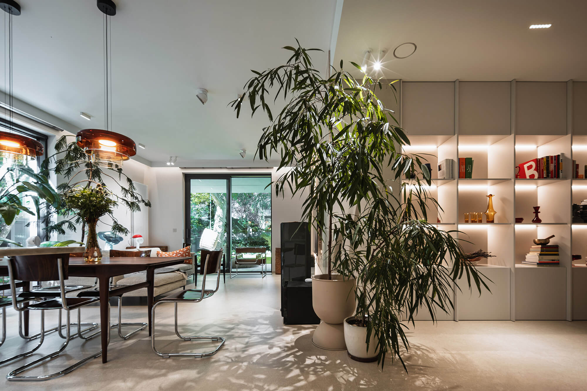 Wnętrze nowoczesnego salonu z roślinami, regałem i stołem jadalnym. Jasne, przestronne mieszkanie.