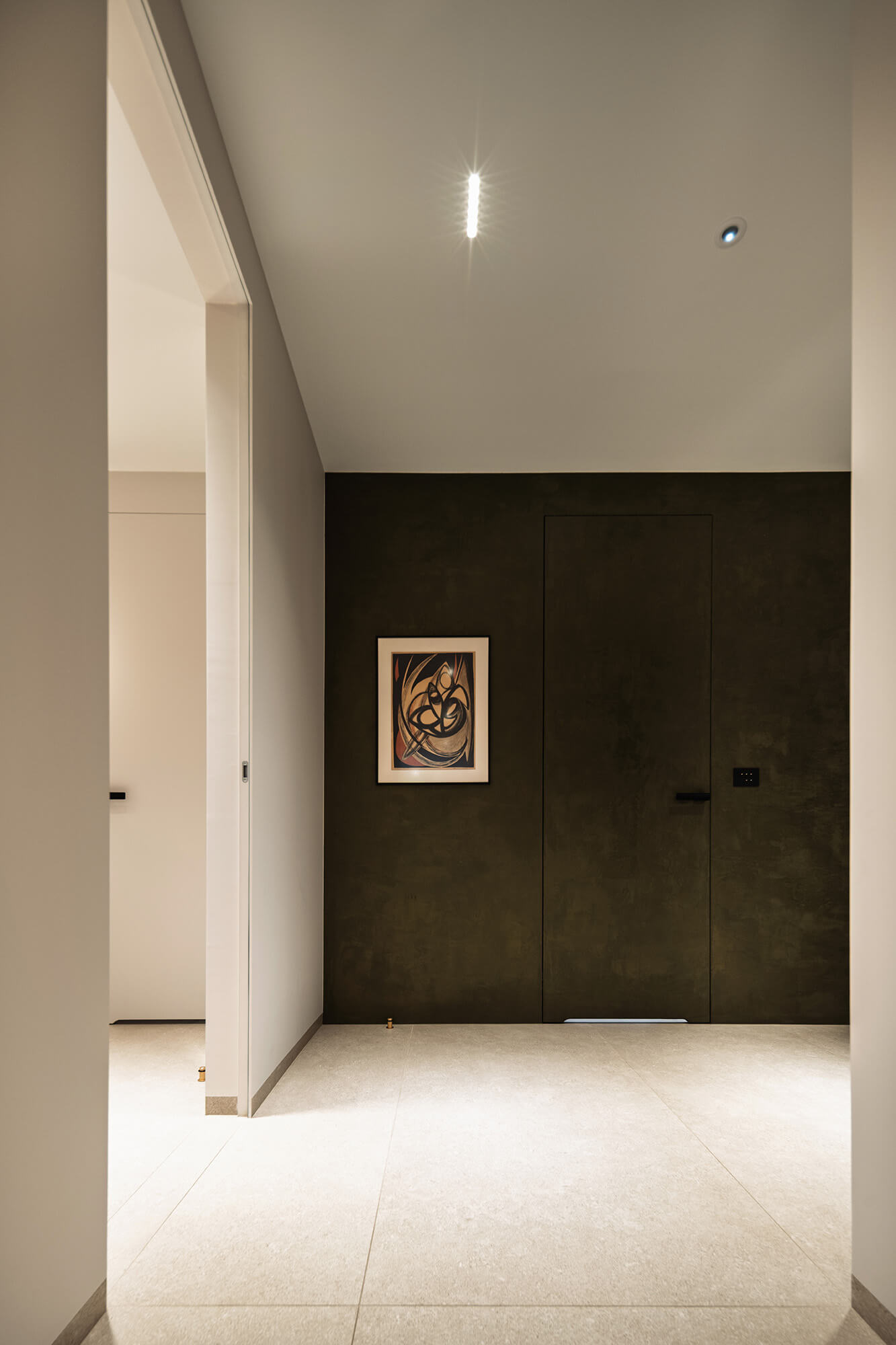 Nowoczesny korytarz z obrazem i ukrytymi drzwiami w ciemnej ścianie.