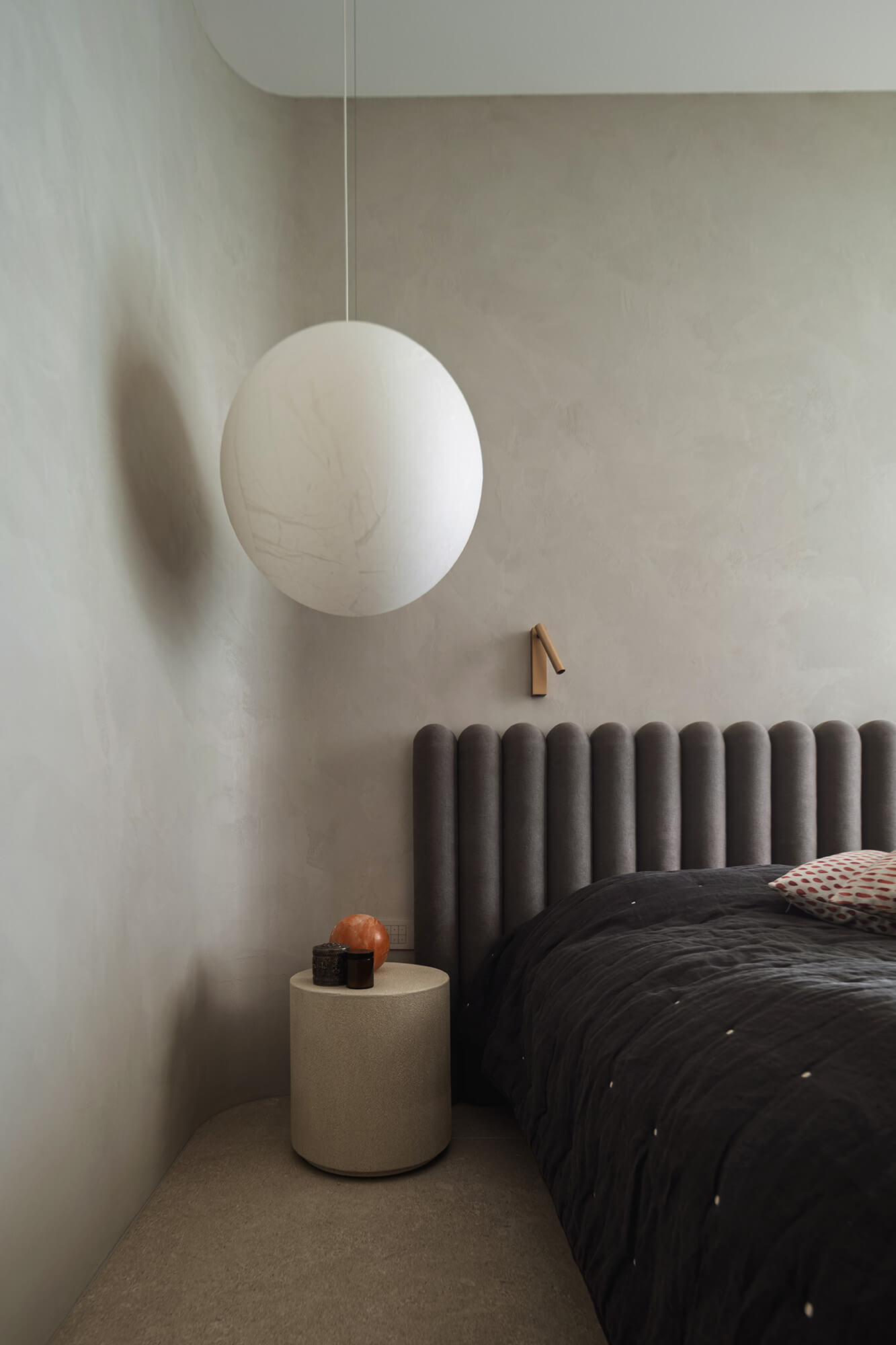 Sypialnia w neutralnych barwach: okrągła lampa, łóżko z wezgłowiem i stolik nocny.