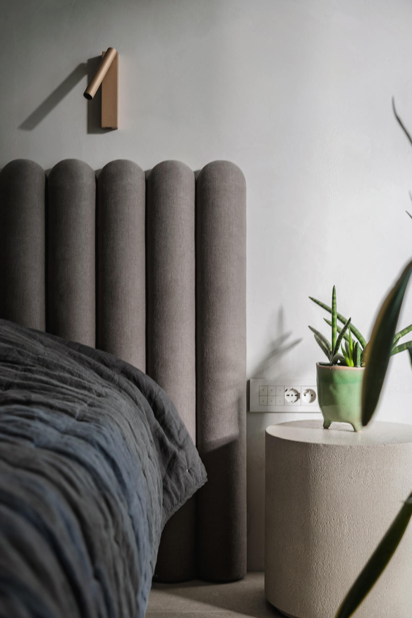 Nowoczesna sypialnia: szare łóżko z zagłówkiem, roślina w doniczce na stoliku nocnym.