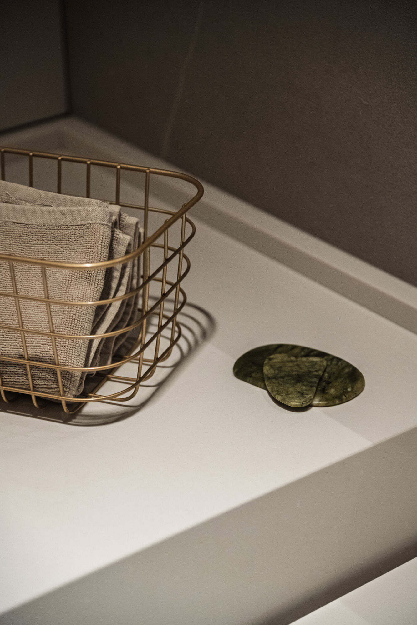 Kosz z ręcznikami i kamienie gua sha na białym blacie.