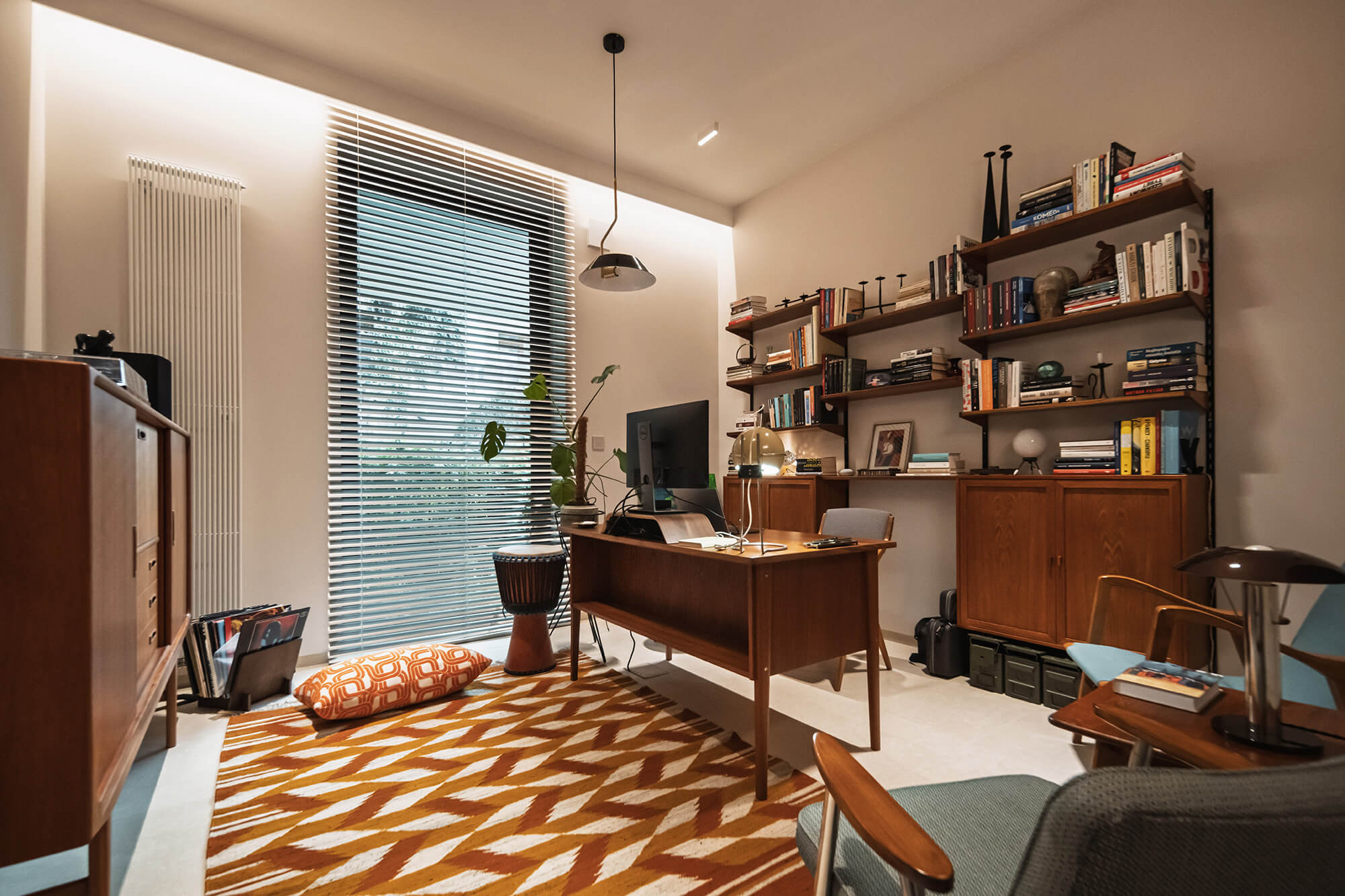 Nowoczesne biuro domowe z drewnianymi meblami w stylu vintage, dywanem w geometryczne wzory i regałem z książkami.