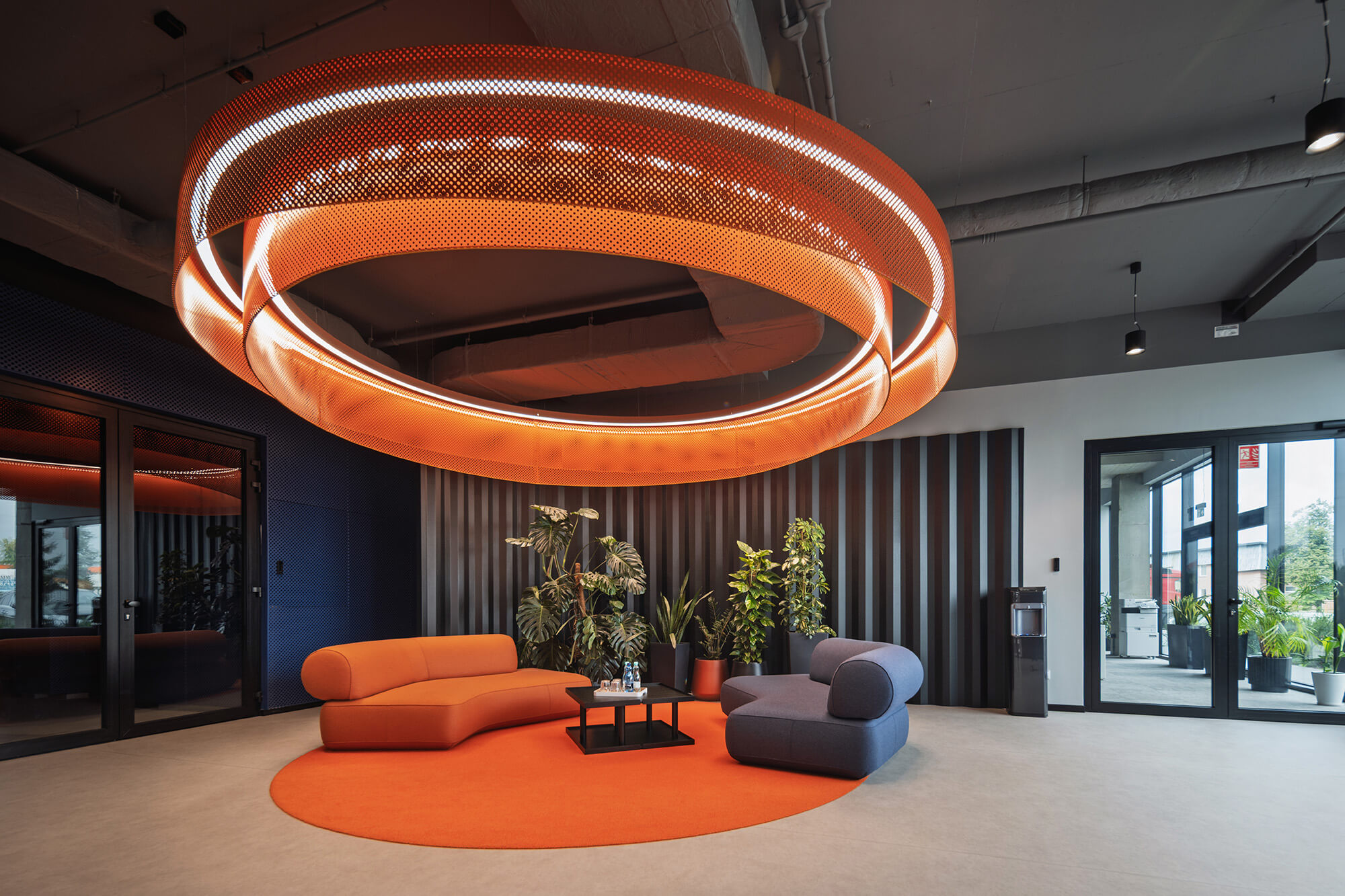 Nowoczesne biuro: pomarańczowa lampa, sofa i fotel na okrągłym dywanie.