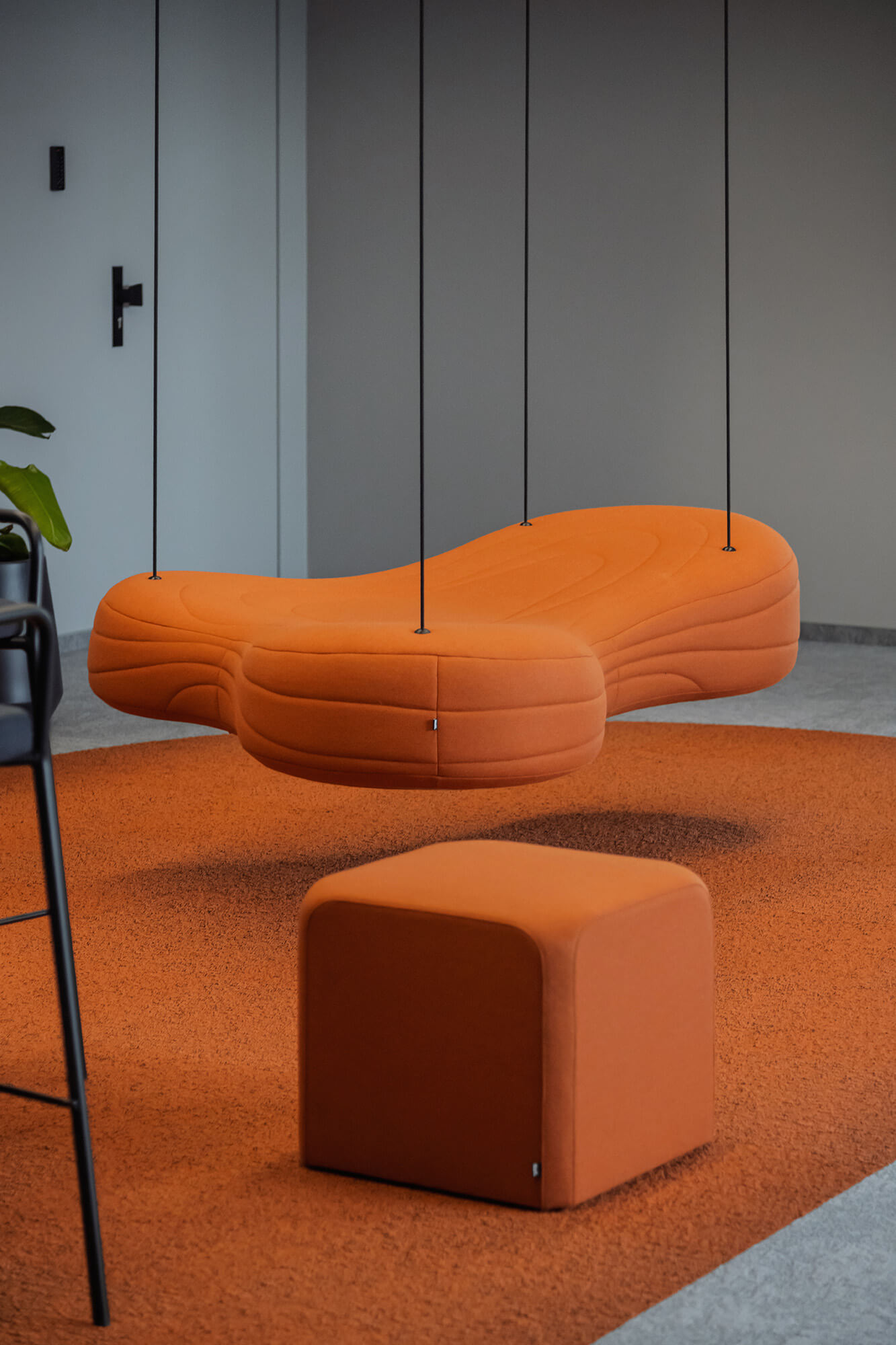 Pomarańczowa, wisząca sofa i pufa na pomarańczowym dywanie. Nowoczesne wnętrze /008k overis.