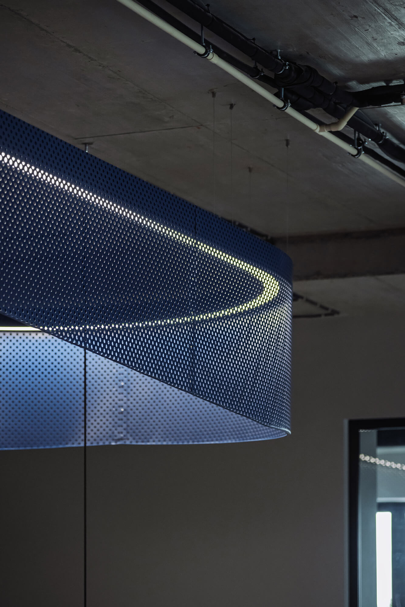 Niebieska, perforowana lampa wisząca na tle betonowego sufitu. /008k overis