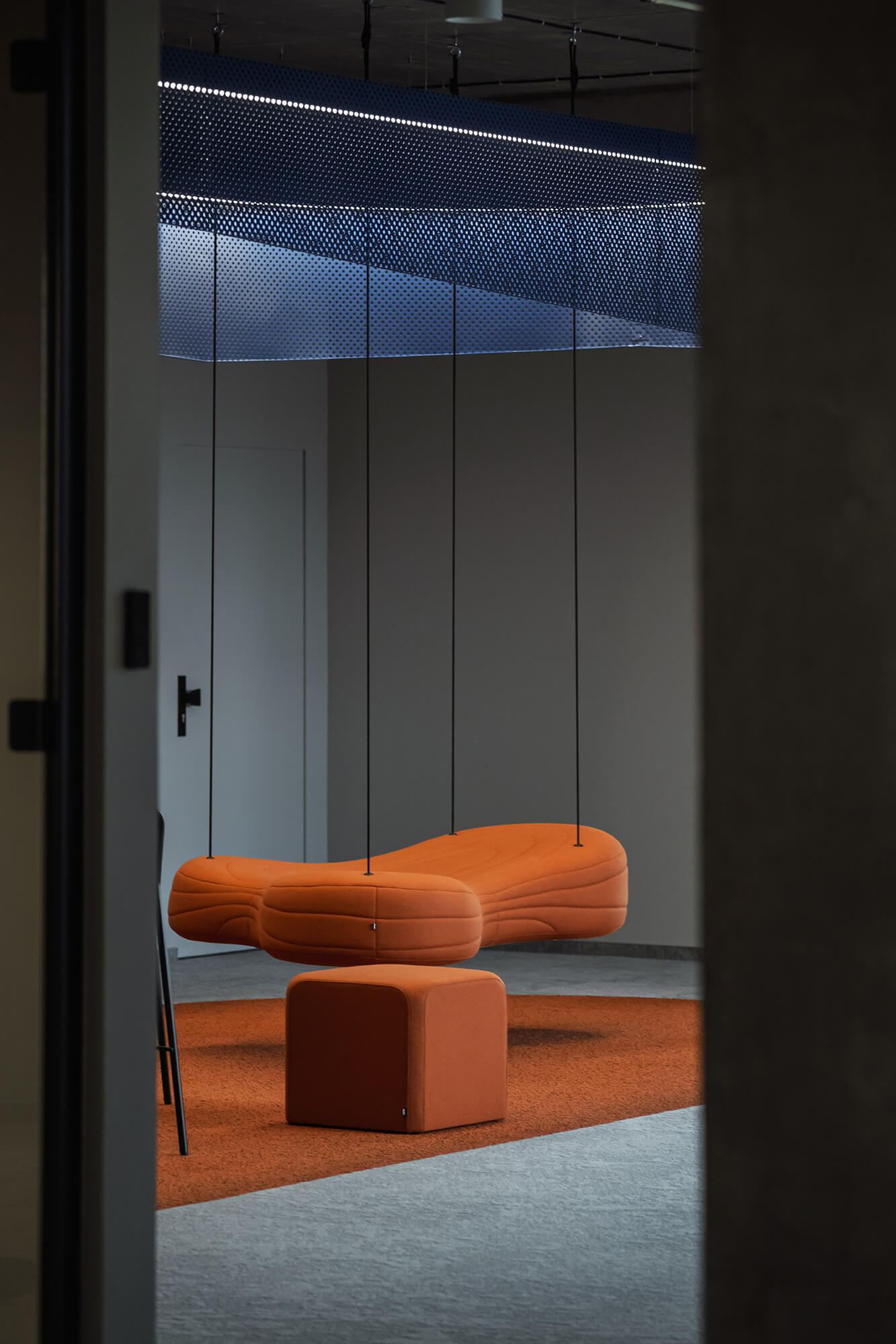 Pomarańczowa wisząca sofa i pufa w nowoczesnym wnętrzu.