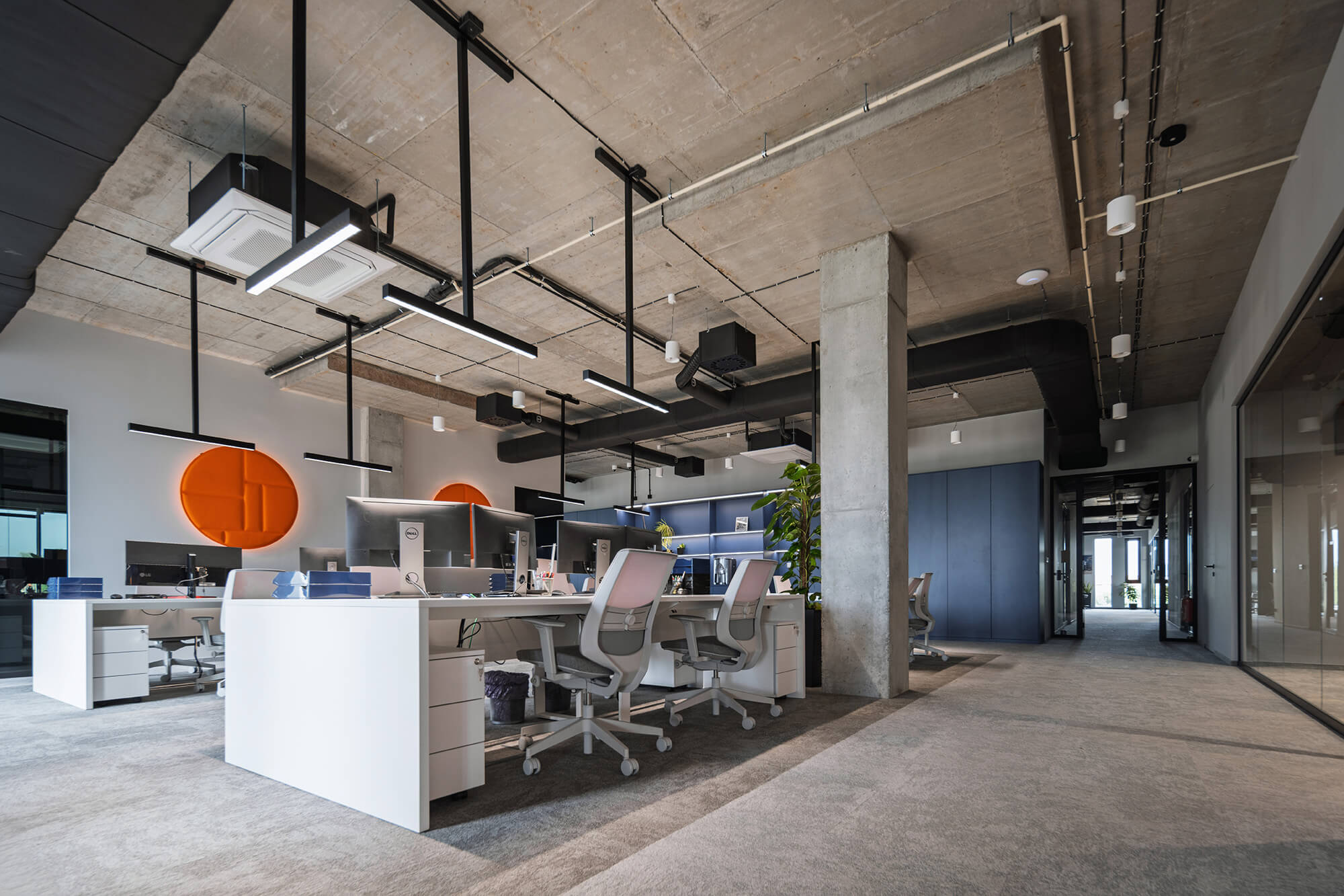 Nowoczesne biuro z surowym betonowym sufitem, białymi biurkami i szarymi krzesłami. Oświetlenie liniowe LED.