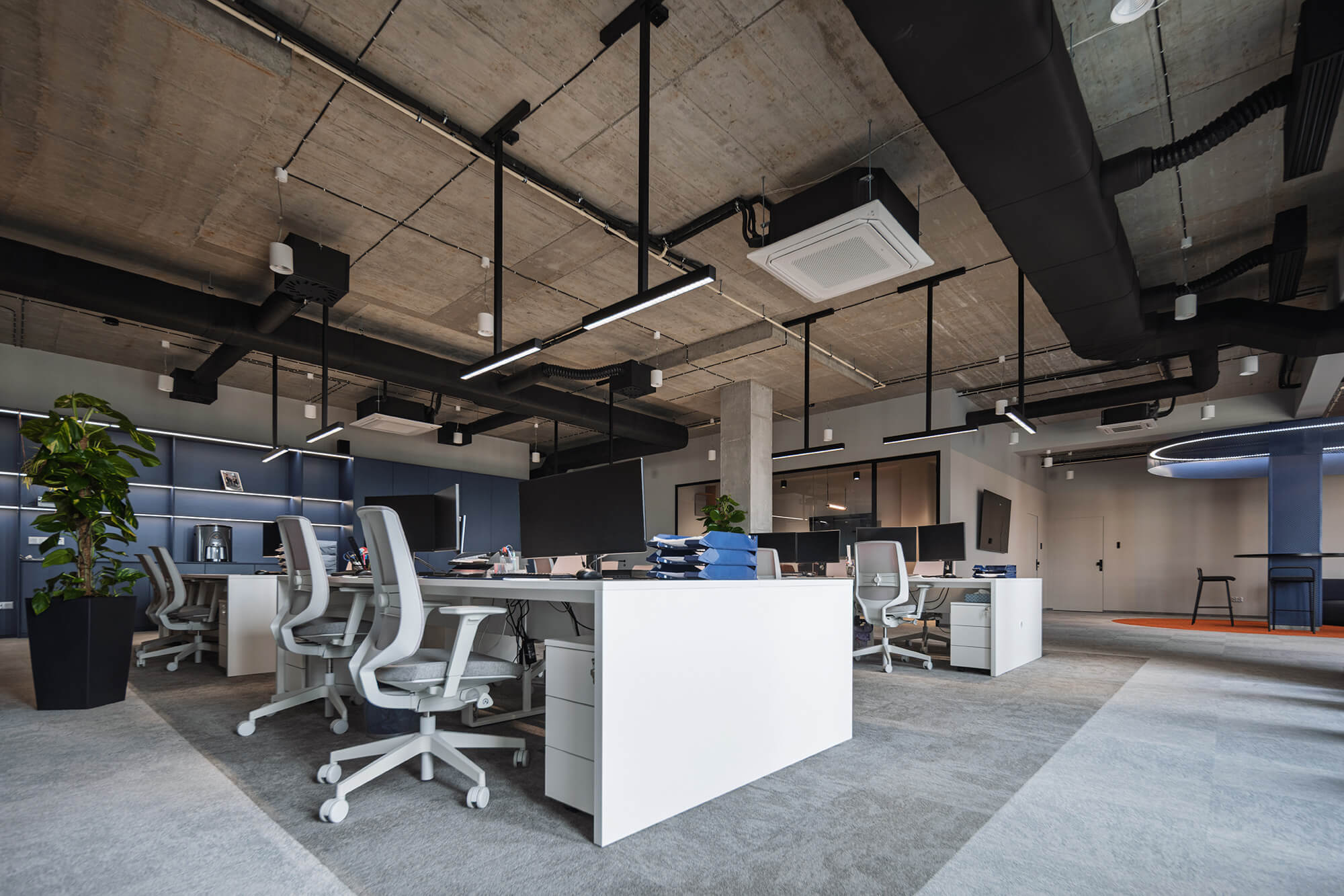 Nowoczesne biuro z betonowym sufitem, białymi biurkami i szarymi krzesłami.