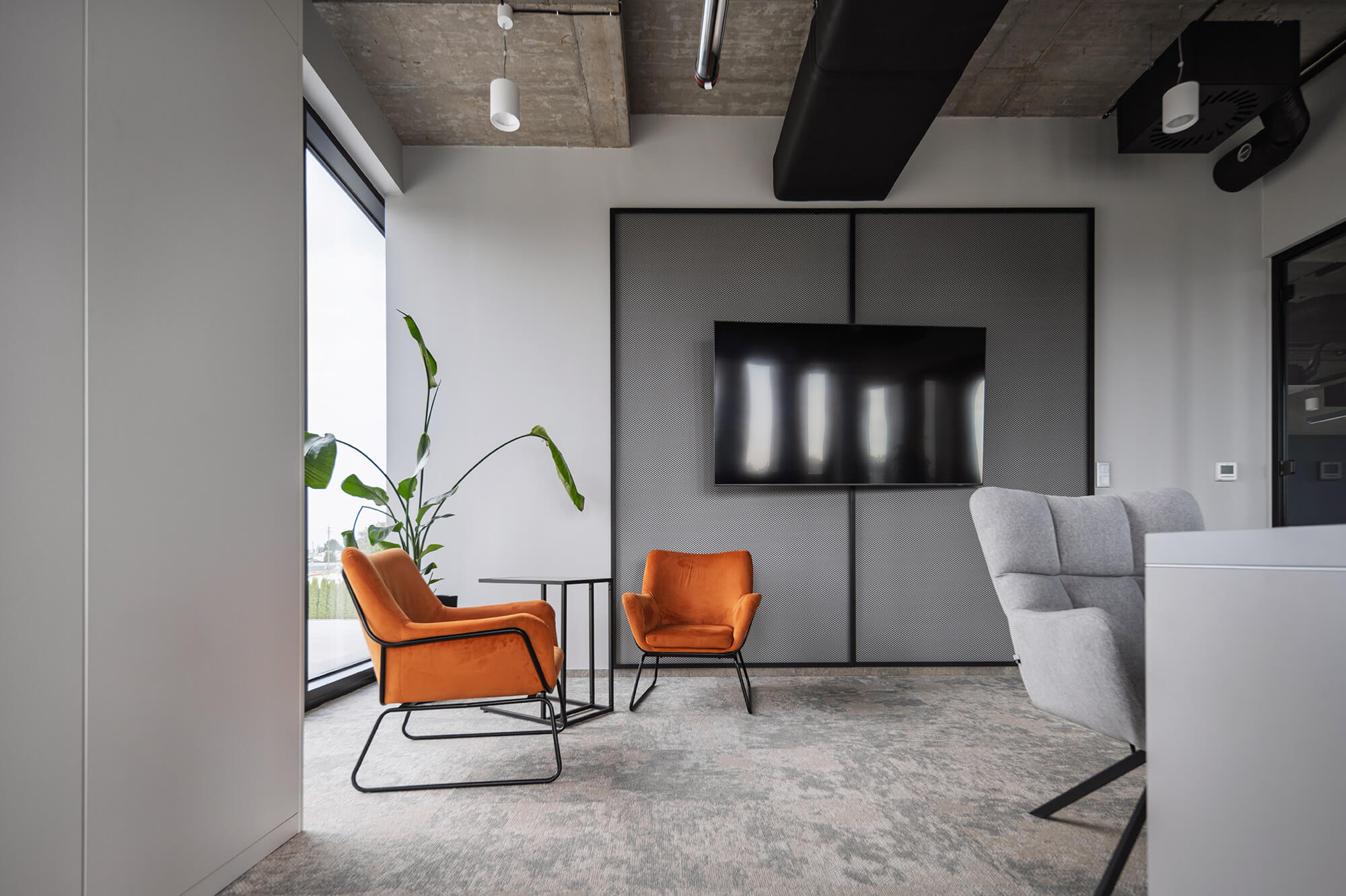 Nowoczesny salon biurowy z pomarańczowymi krzesłami i telewizorem na ścianie