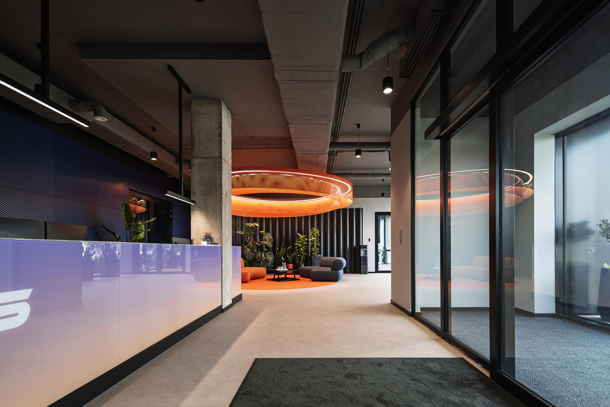 Recepcja biura z nowoczesnym designem, pomarańczowym oświetleniem i elementami betonu.
