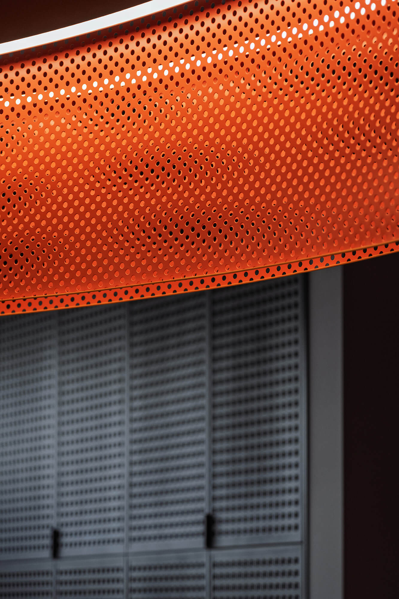 Zakrzywiona, pomarańczowa, perforowana konstrukcja z metalową siatką w tle