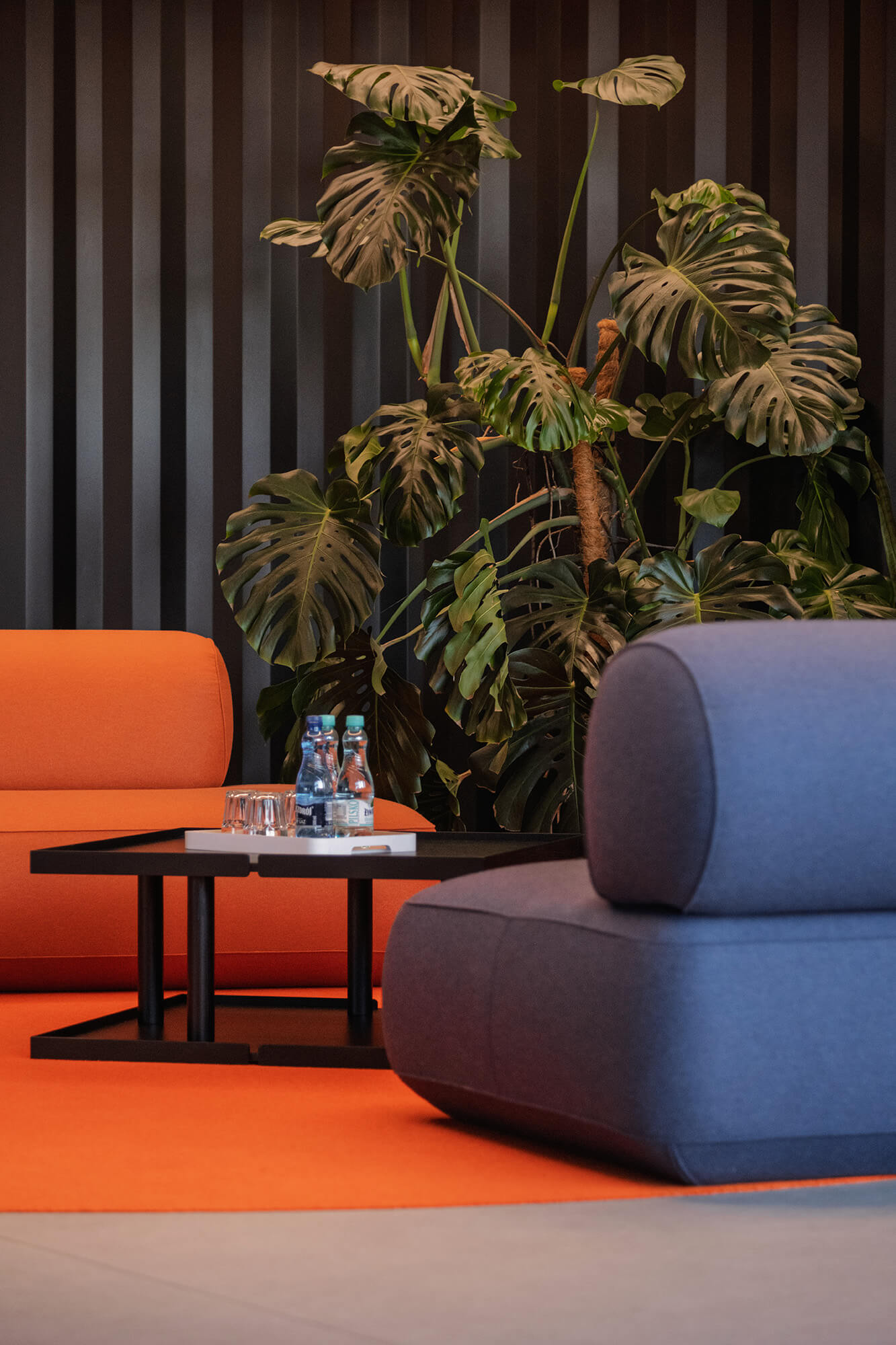 Stylowe wnętrze z pomarańczową sofą, szarym fotelem i monsterą. Minimalistyczny design.