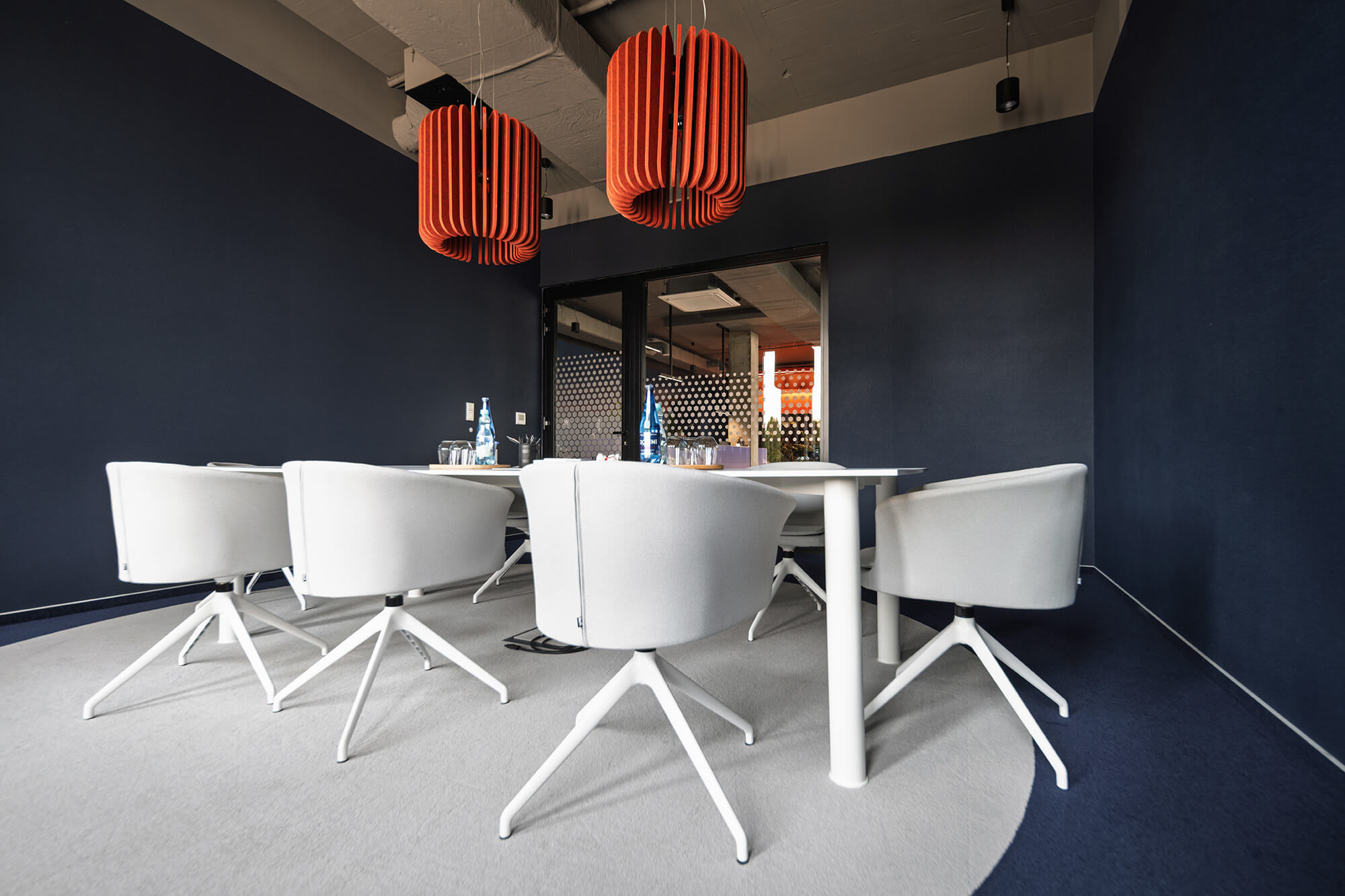 Sala konferencyjna z białym stołem, krzesłami i pomarańczowymi lampami.