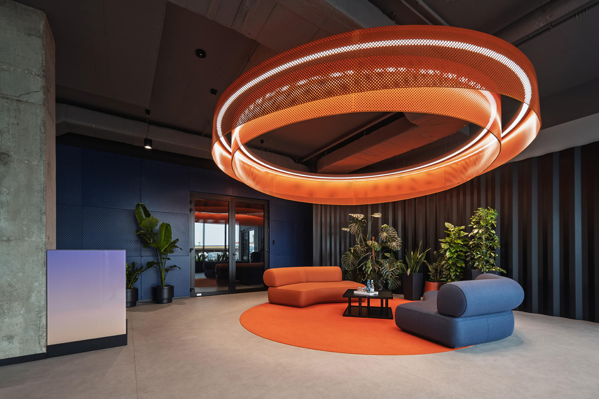 Nowoczesne biuro: pomarańczowy żyrandol, niebieskie sofy, rośliny doniczkowe.