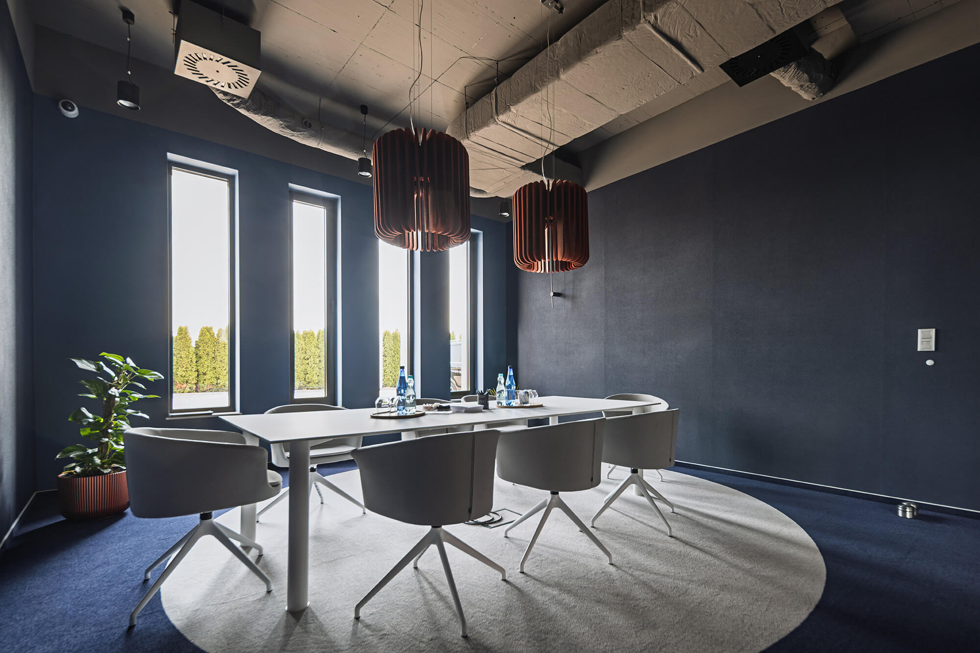 Sala konferencyjna z minimalistycznym stołem, krzesłami i oknami.