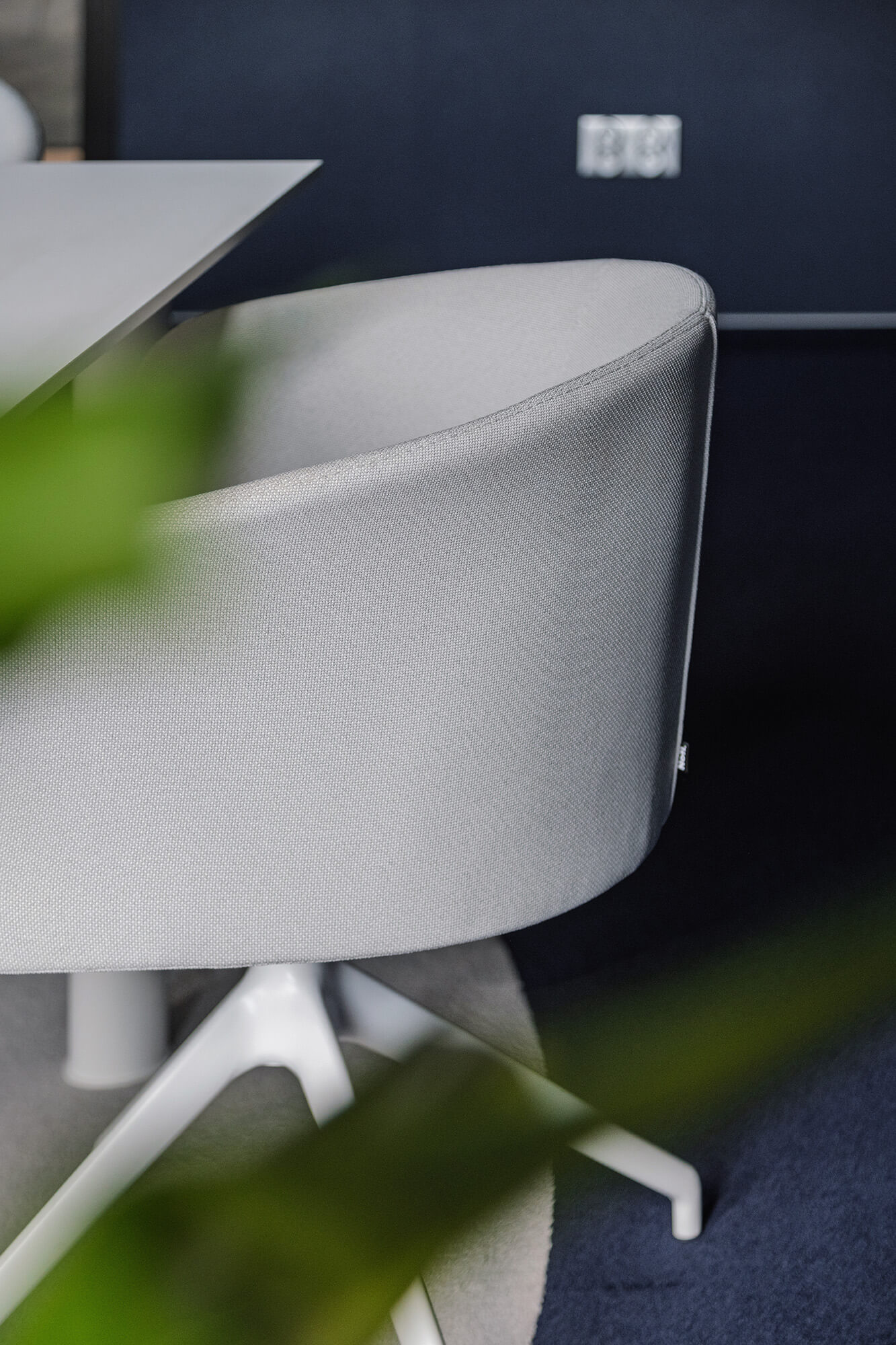 Szczegół krzesła biurowego z białą tapicerką i białym stelażem na tle ciemnej ściany.