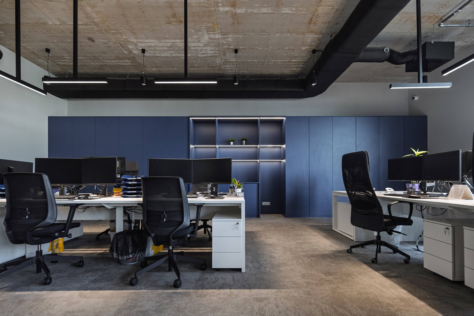 Nowoczesne biuro z białymi biurkami, czarnymi krzesłami i niebieską szafą.