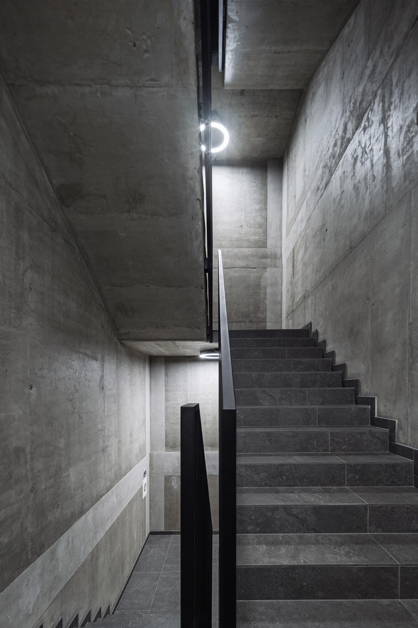 Betonowe schody w nowoczesnym budynku, oświetlone okrągłymi lampami. Minimalizm i surowość architektury.