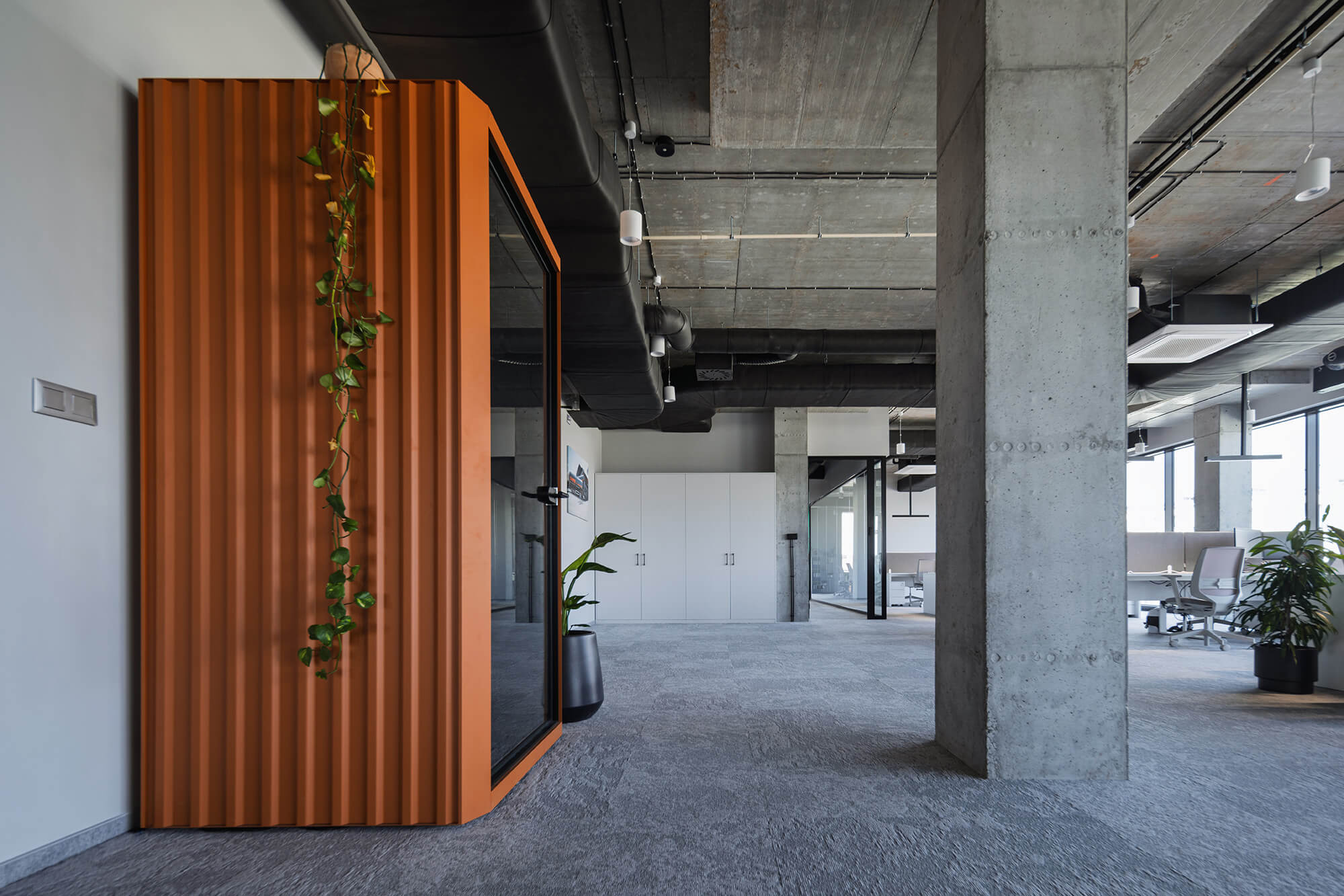 Nowoczesne biuro z betonowymi kolumnami, kabiną akustyczną i roślinami. Minimalistyczny design.