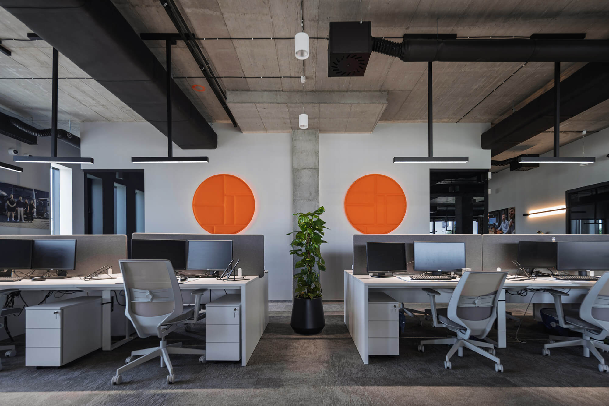 Nowoczesne biuro z białymi biurkami, szarymi krzesłami i pomarańczowymi dekoracjami na ścianie.