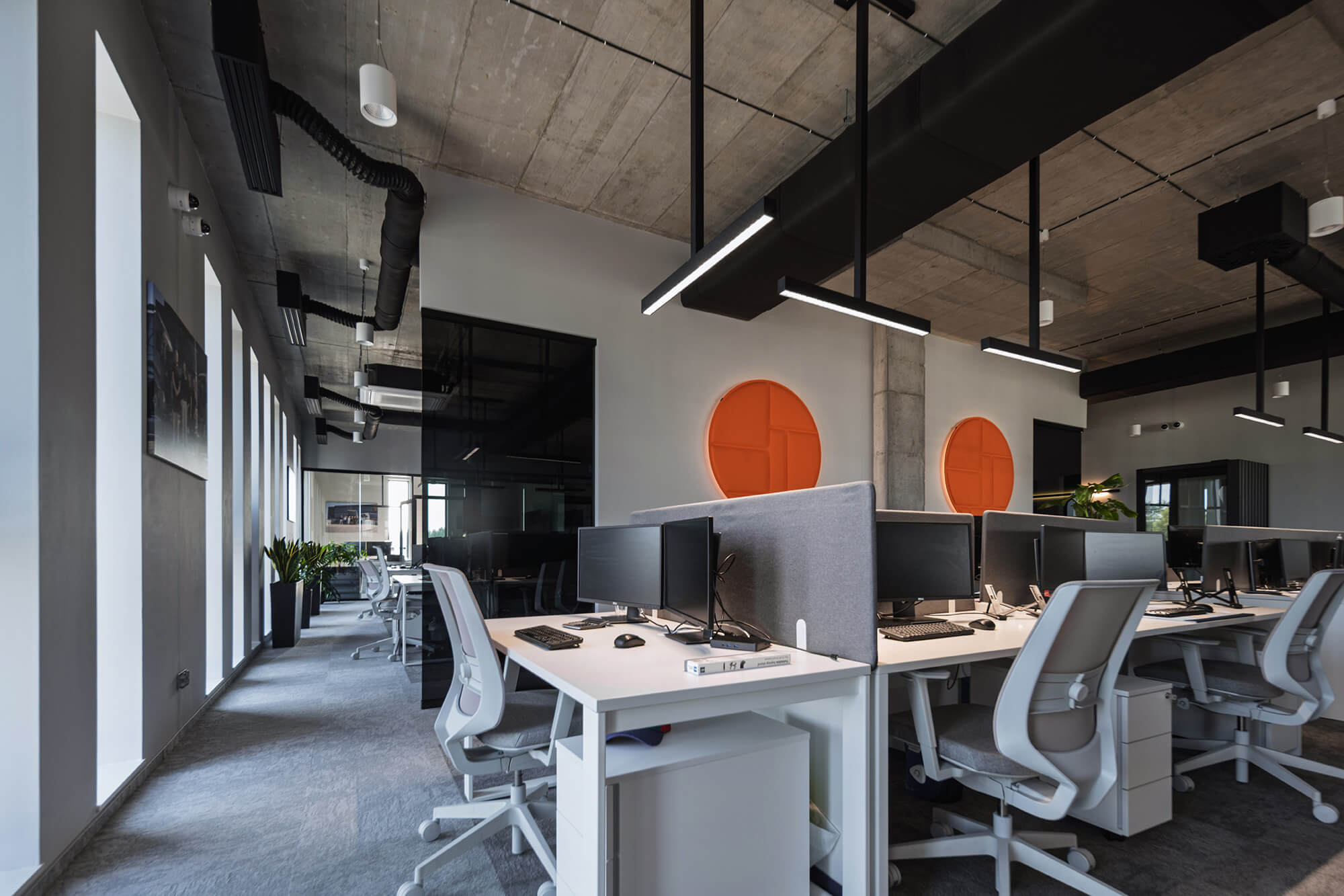 Nowoczesne biuro z szarymi dywanami, białymi biurkami i pomarańczowymi akcentami.