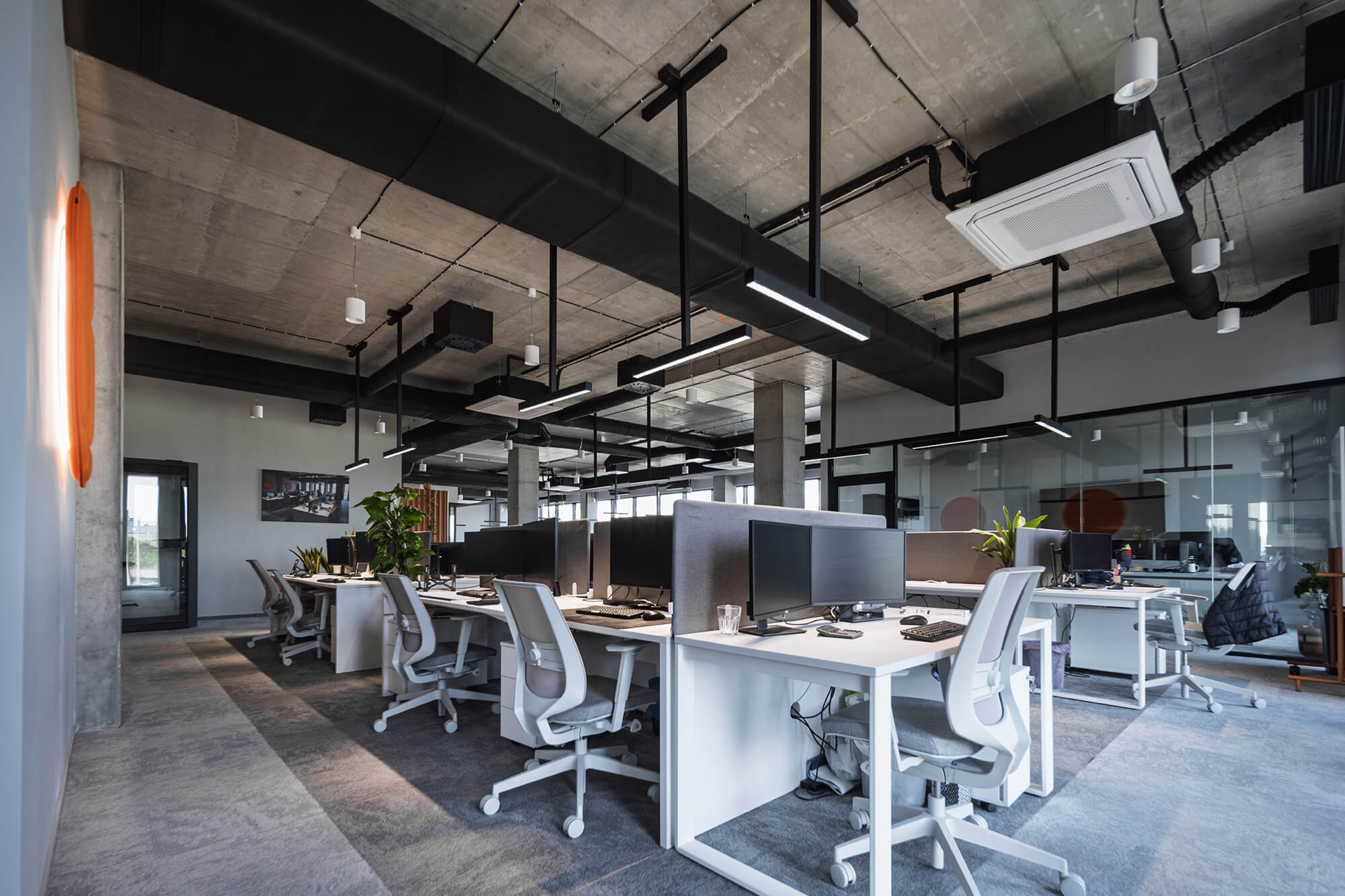 Nowoczesne biuro z surowym betonowym sufitem i białymi biurkami.