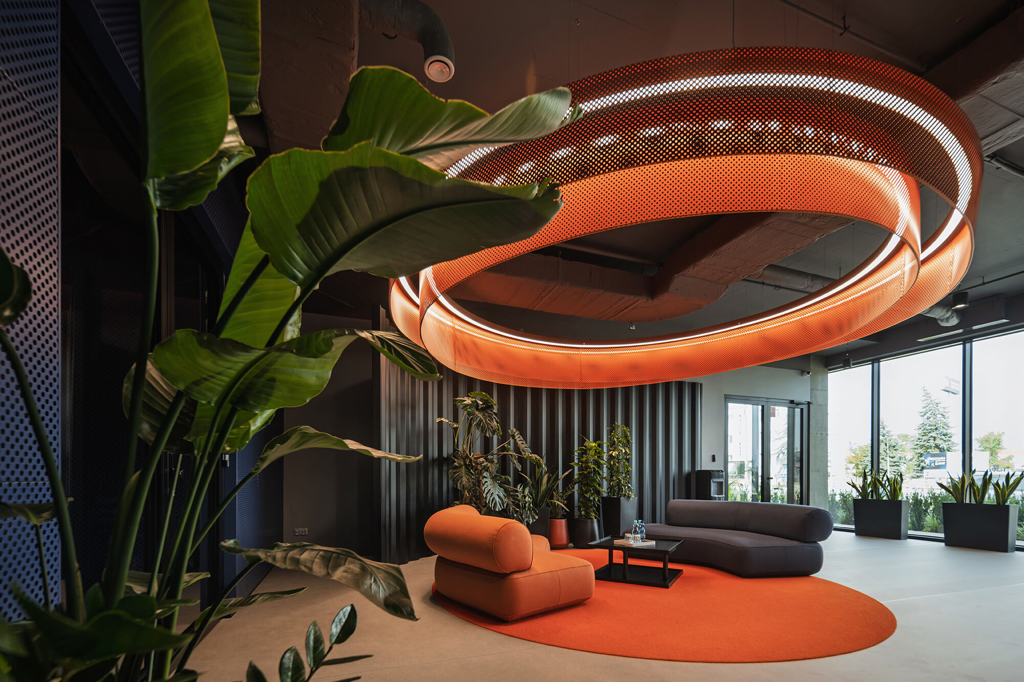 Nowoczesne wnętrze biurowe z roślinami, pomarańczowym dywanem i okrągłą lampą. Przestrzeń relaksu w /008k overis.