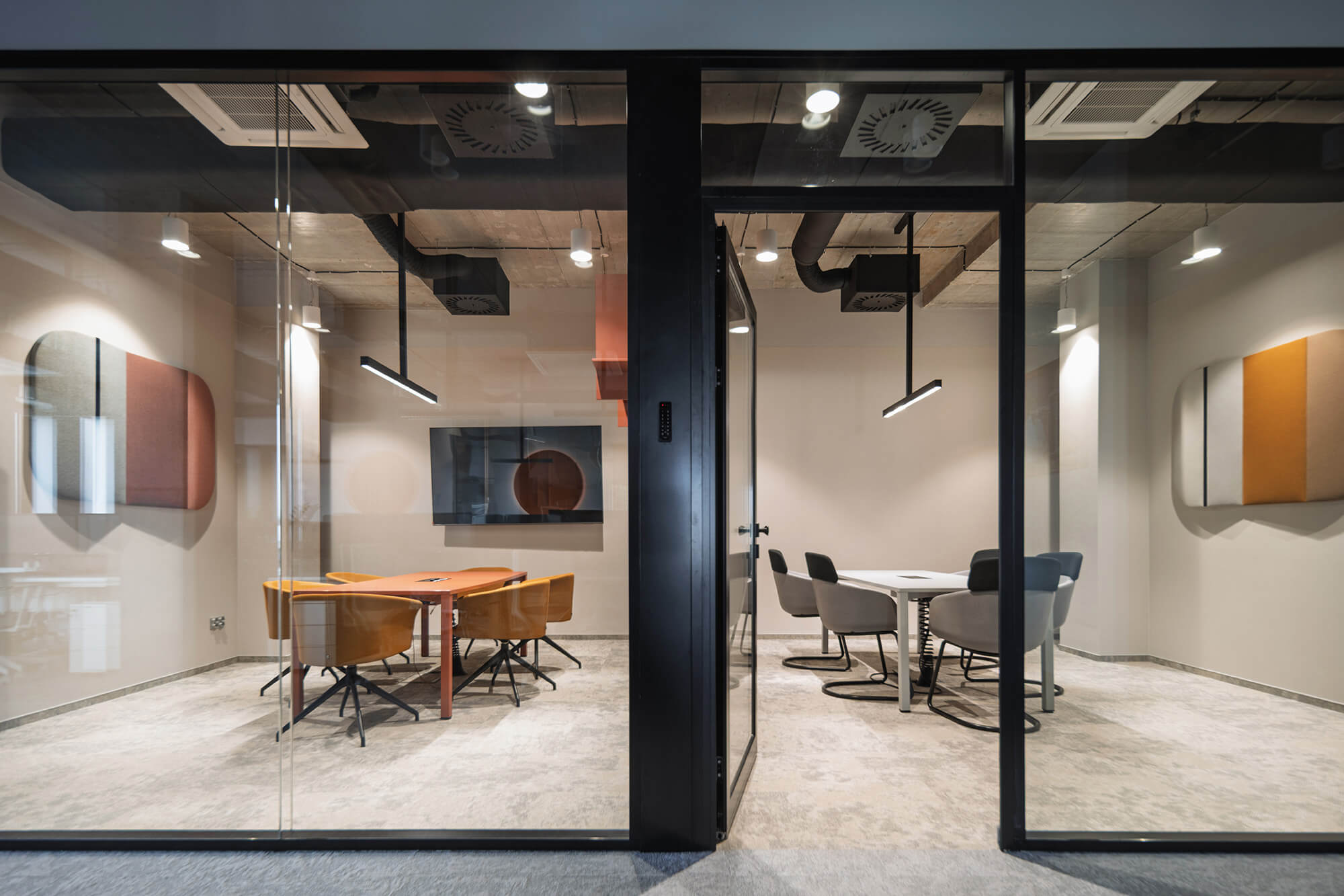 Dwie nowoczesne sale konferencyjne oddzielone szklanymi ścianami. Jedna z pomarańczowymi krzesłami, druga z szarymi.