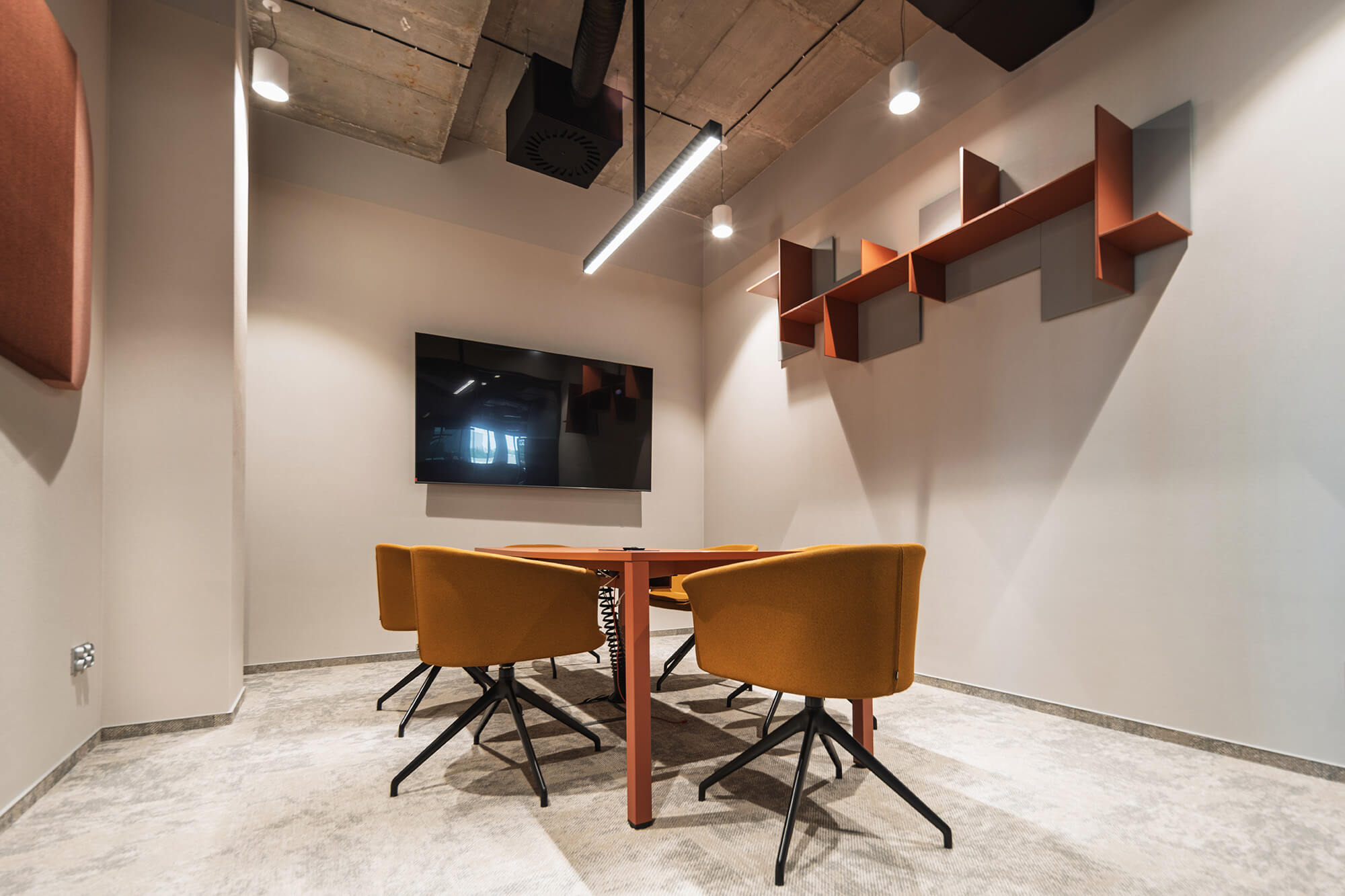 Sala konferencyjna z pomarańczowymi krzesłami i dużym ekranem.