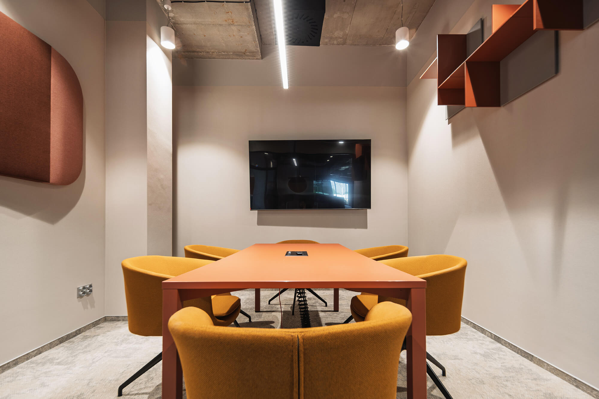 Sala konferencyjna z pomarańczowym stołem i żółtymi krzesłami, nowoczesny wystrój.