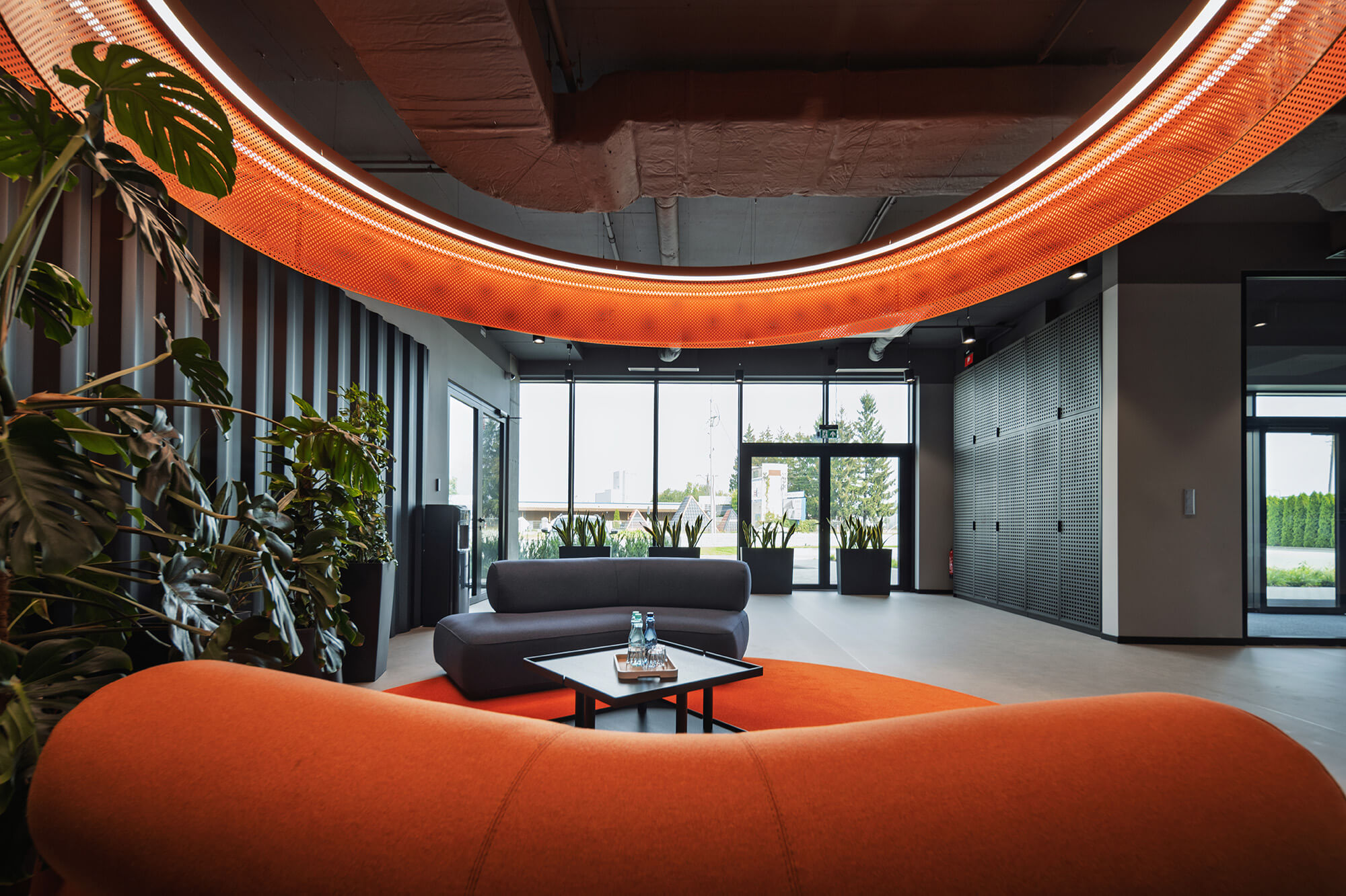 Nowoczesne wnętrze biura z pomarańczową sofą i roślinami. Projekt /008k overis.