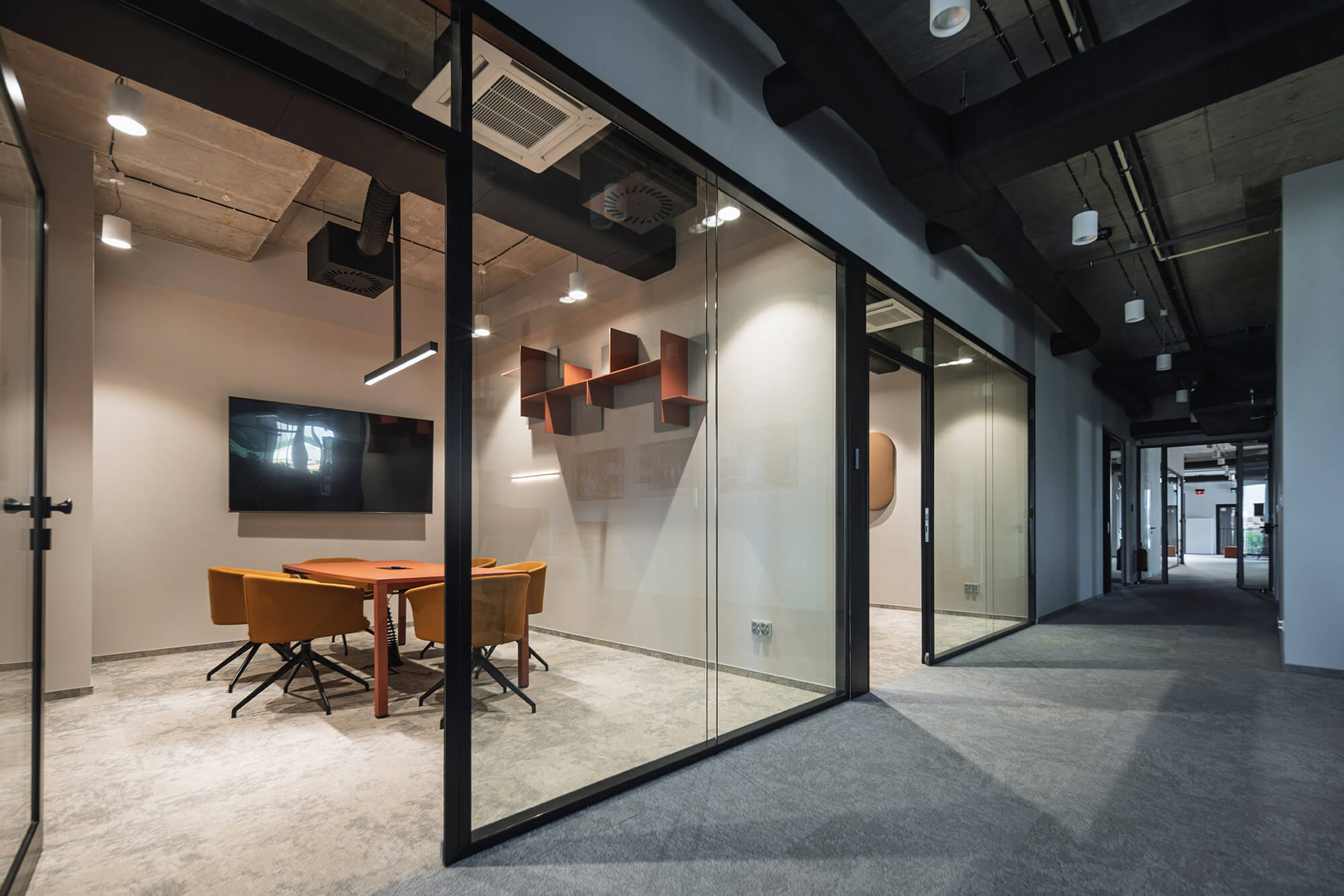 Nowoczesne biuro z przeszklonymi ścianami, sala konferencyjna z pomarańczowym stołem i żółtymi krzesłami.