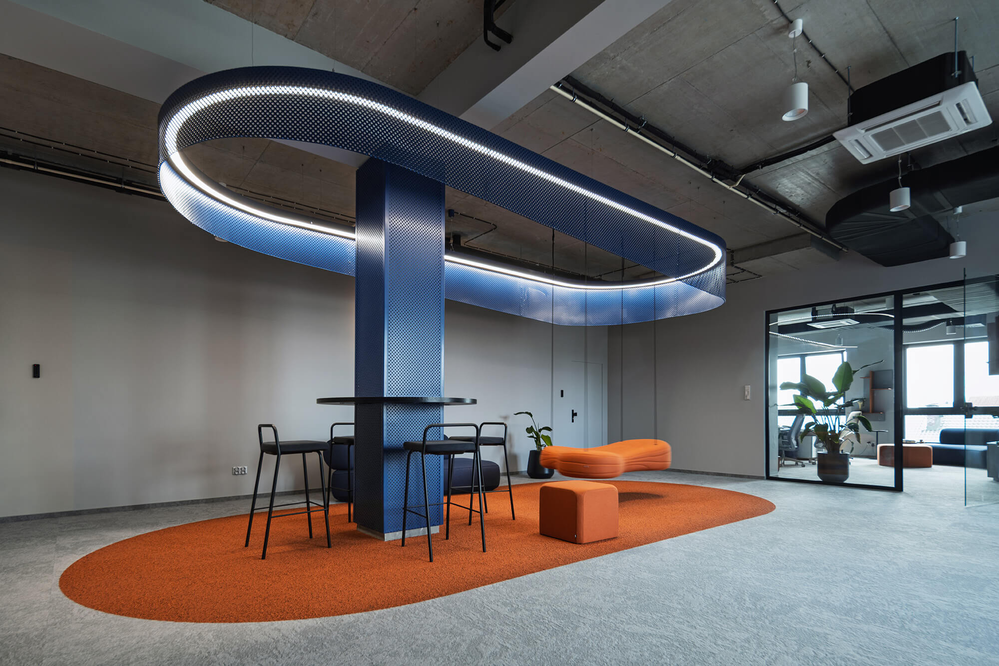 Nowoczesne biuro z niebieską instalacją świetlną nad pomarańczowym dywanem.