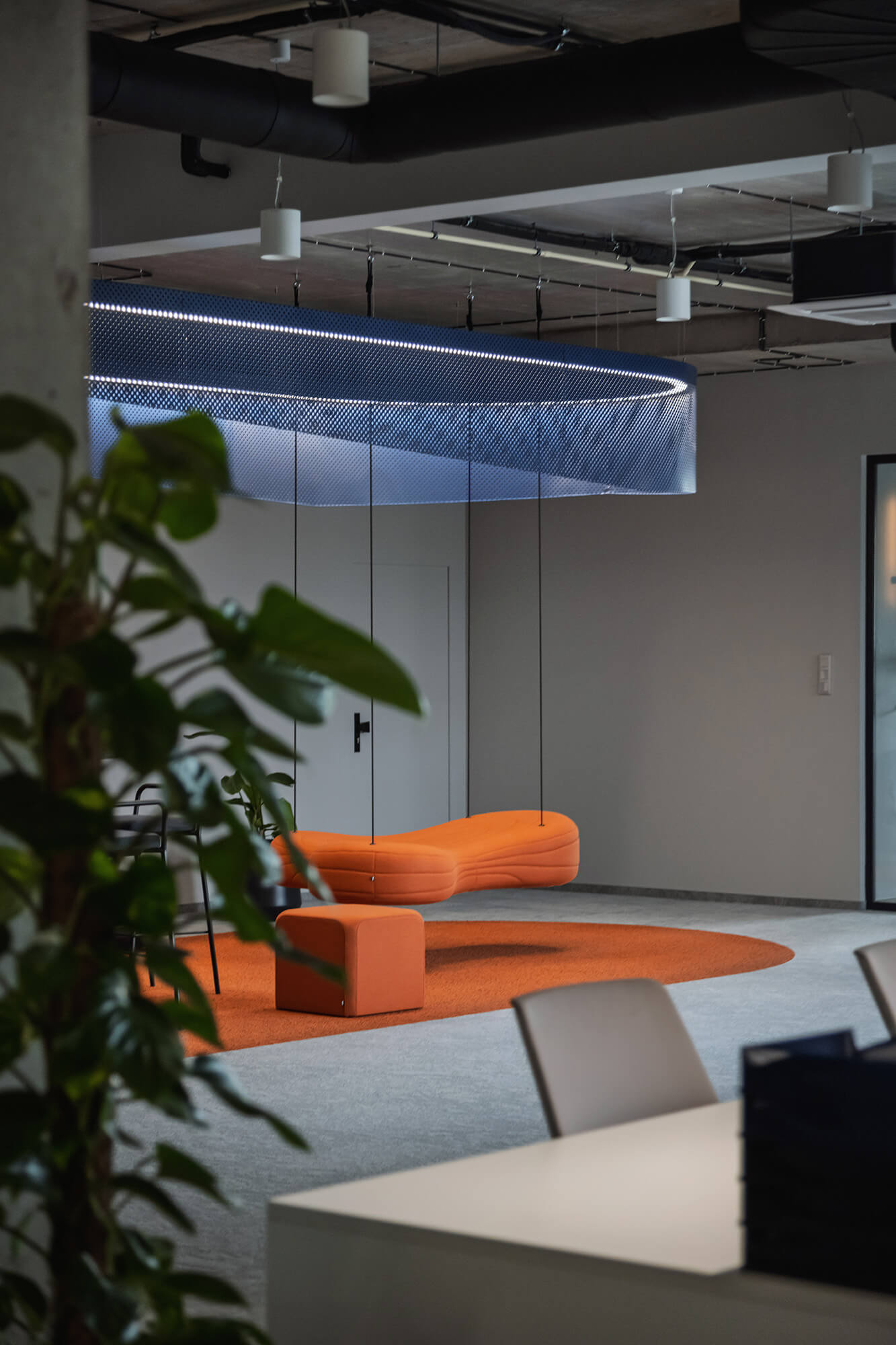 Pomarańczowa sofa podwieszona w nowoczesnym biurze z roślinami. /008k overis