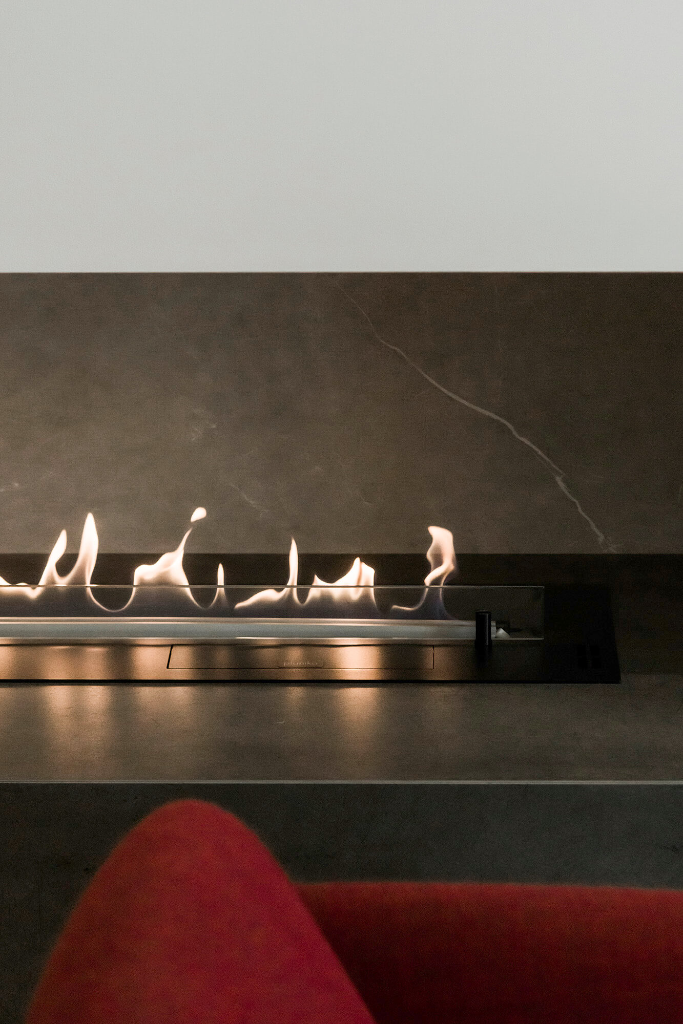 Nowoczesny biokominek z płomieniami na tle szarej ściany.