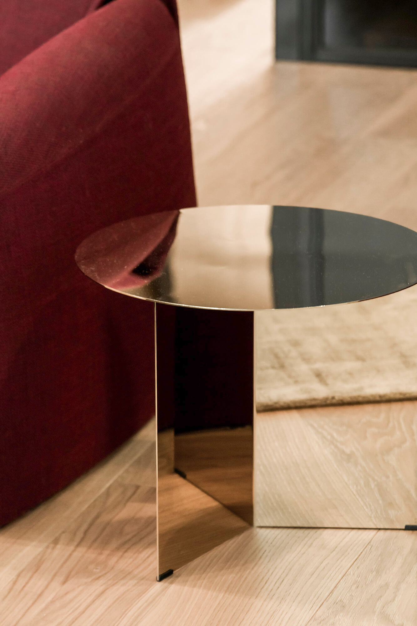 Złoty stolik kawowy obok bordowej sofy na drewnianej podłodze.