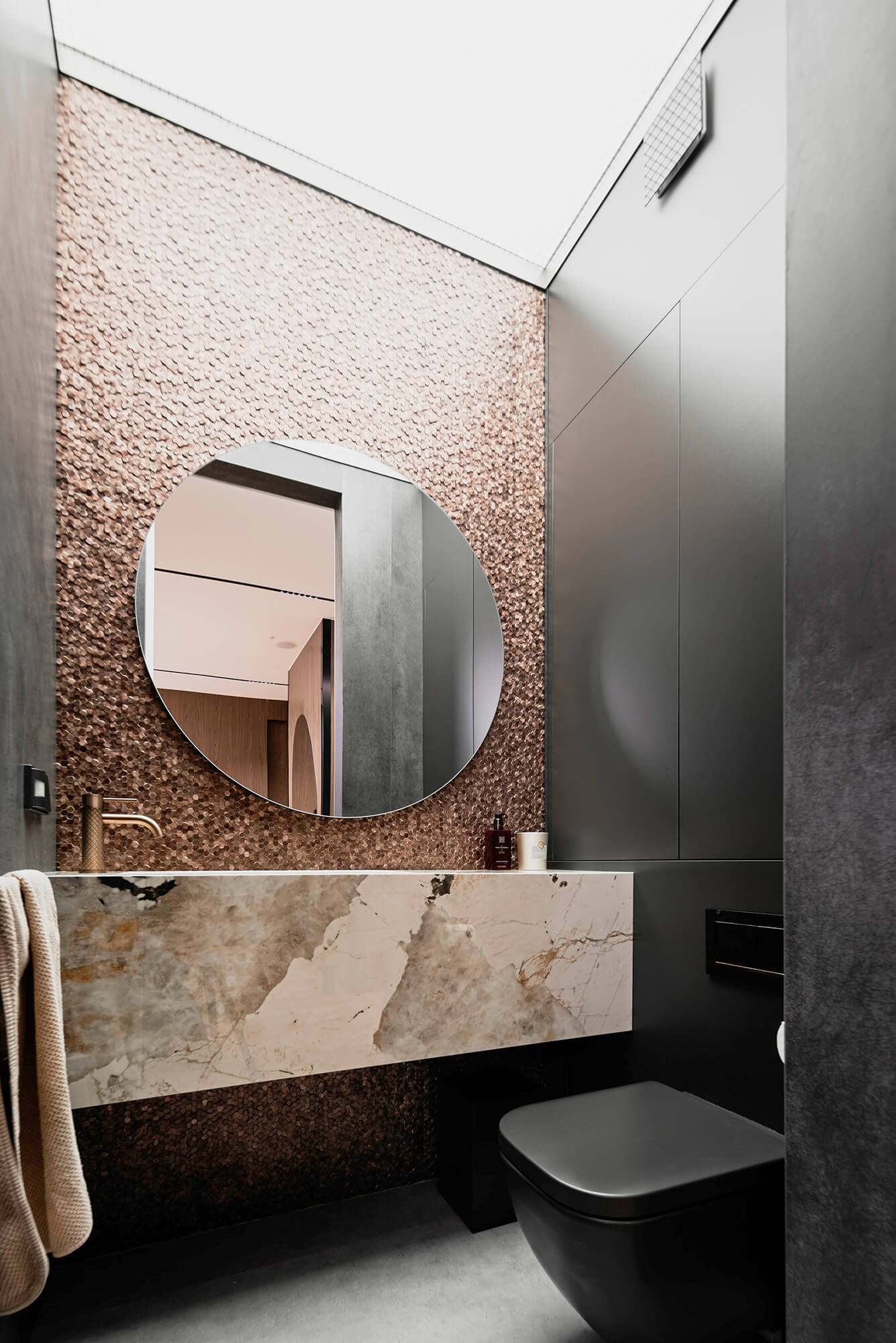 Elegancka łazienka z okrągłym lustrem, marmurową umywalką i czarną toaletą.