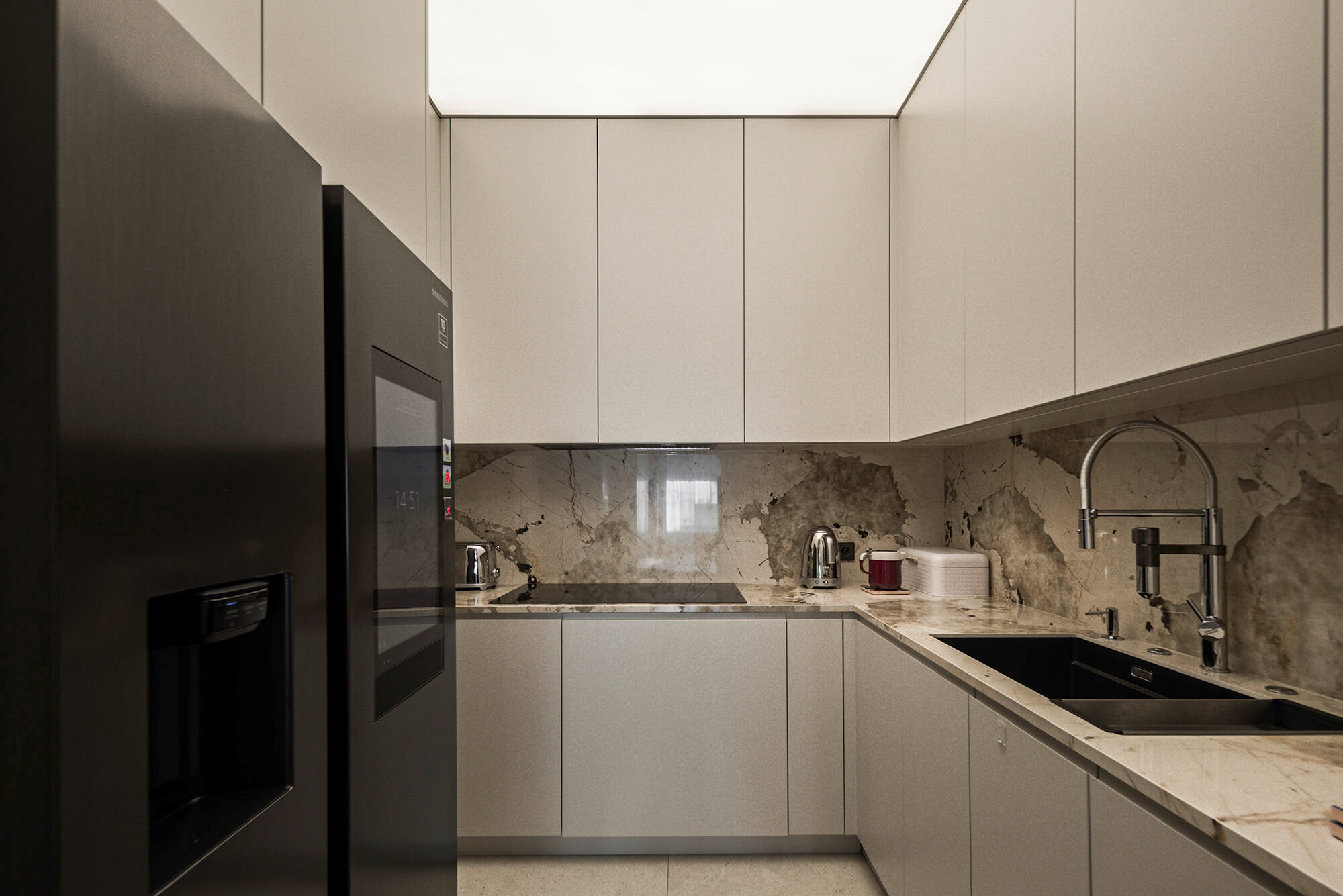 Nowoczesna kuchnia w szarościach: lodówka, szafki i zlewozmywak z marmurowym blatem.