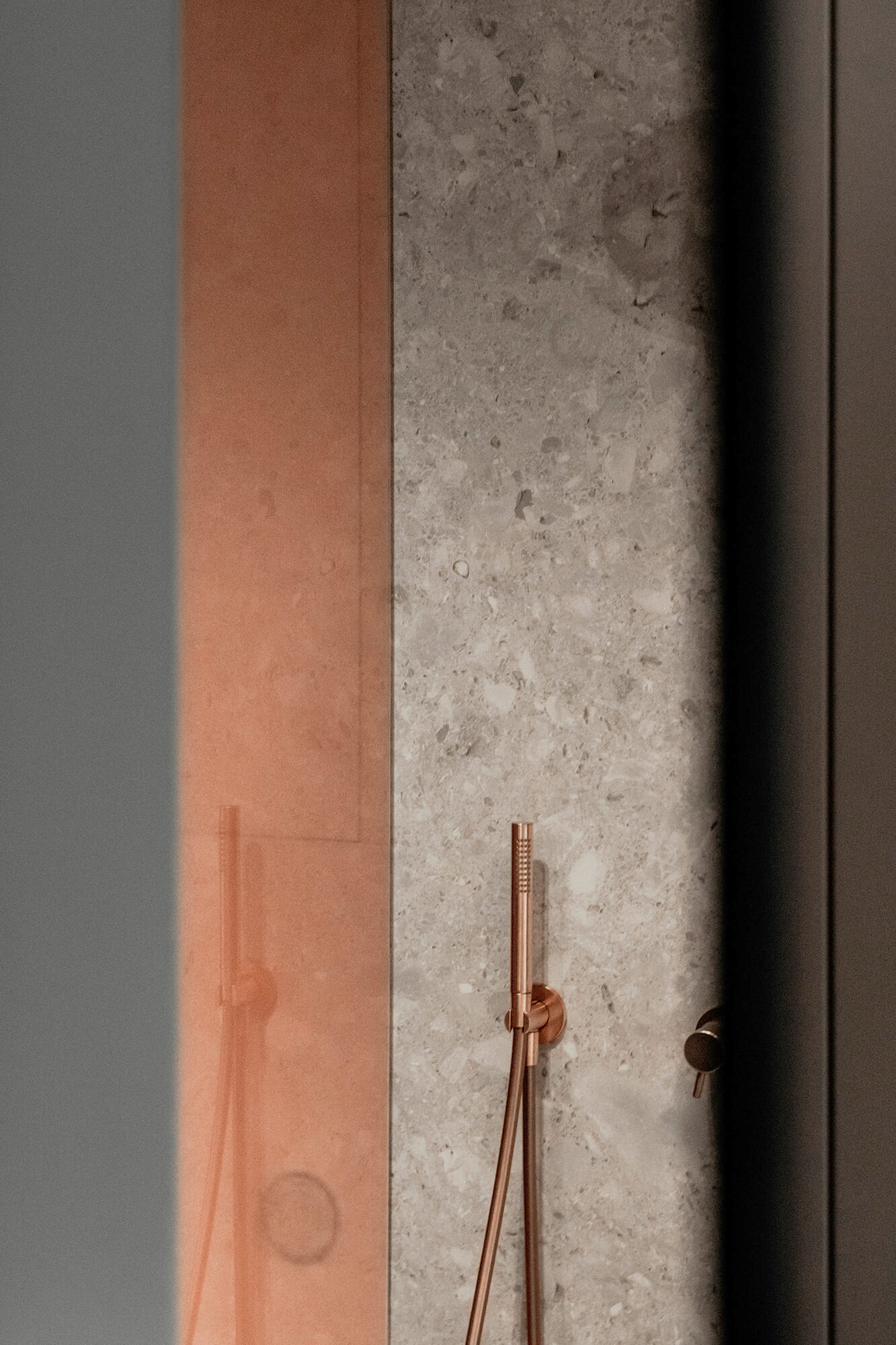 Modern bathroom detail: copper shower fixture against a grey stone wall.