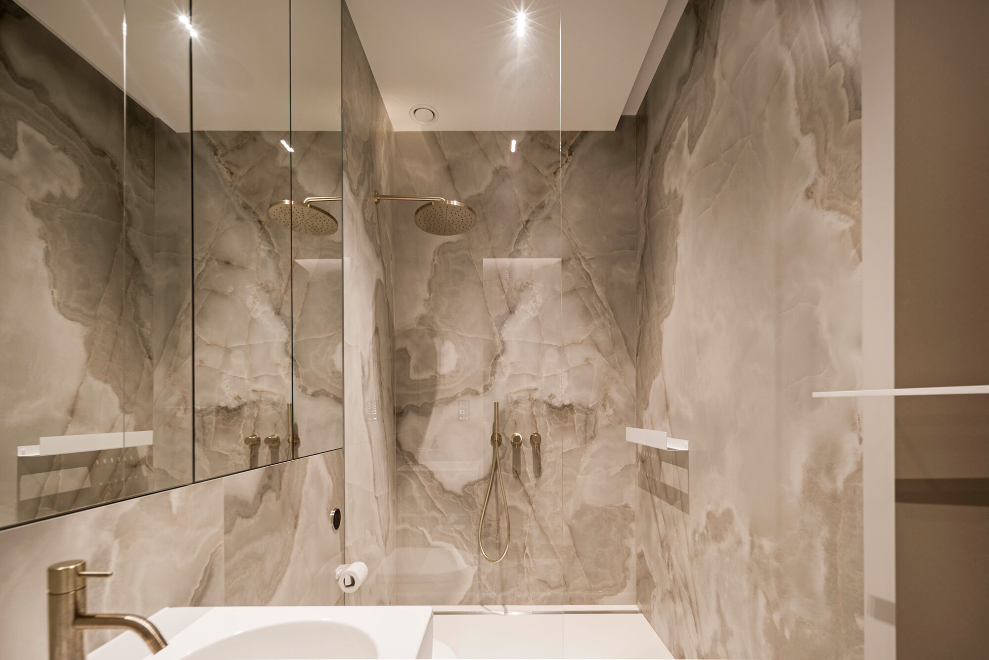 Elegancka łazienka z marmurowymi ścianami, złotą armaturą i szklanym prysznicem.