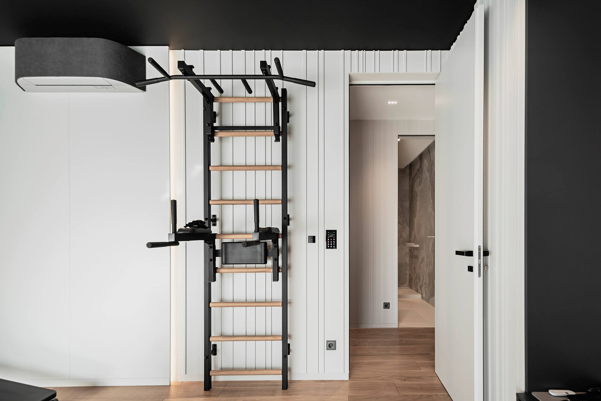 Drabinka gimnastyczna w nowoczesnym wnętrzu z drewnianą podłogą i czarno-białą kolorystyką.