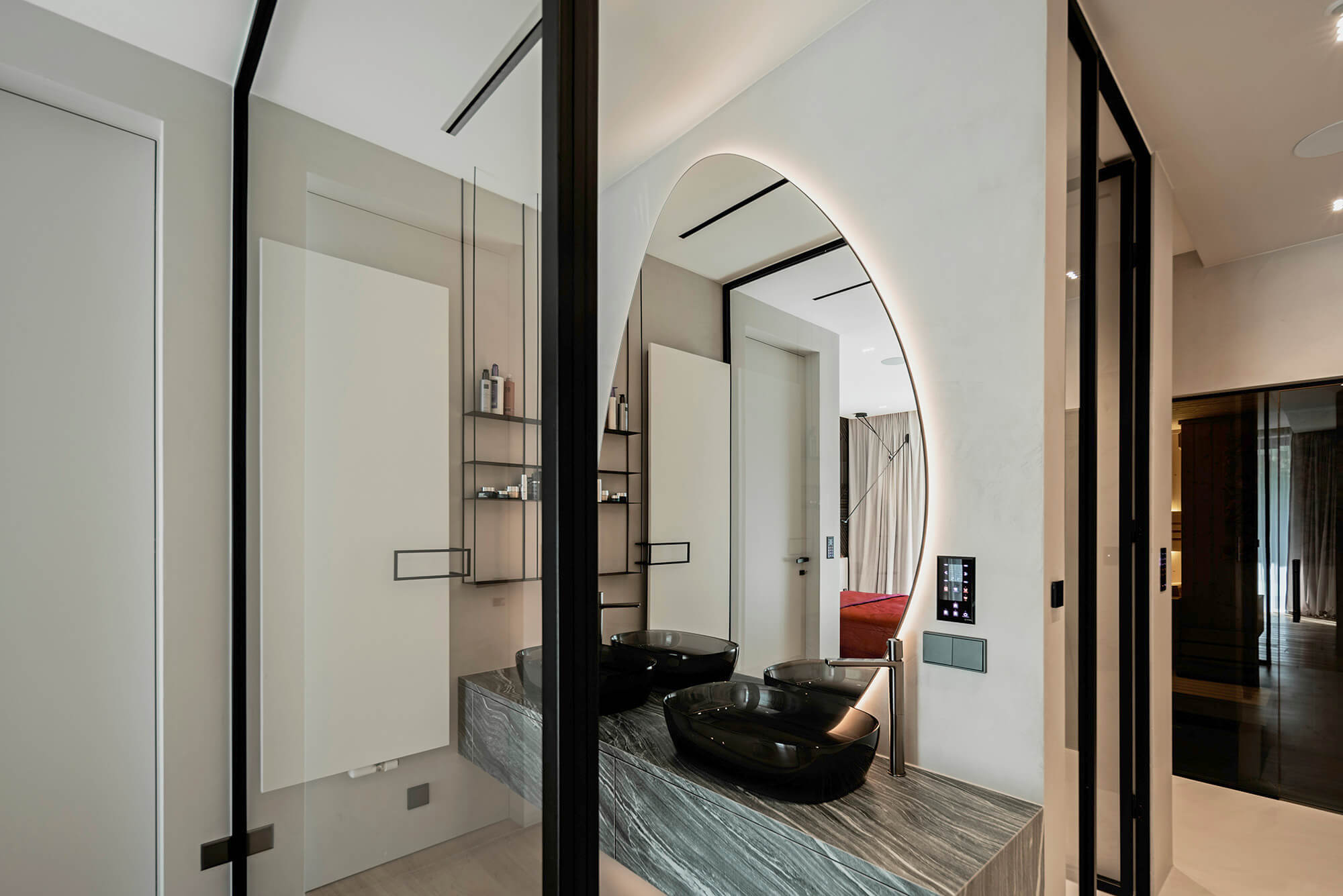 Nowoczesna łazienka z asymetrycznym lustrem, czarnymi umywalkami i szarym blatem.