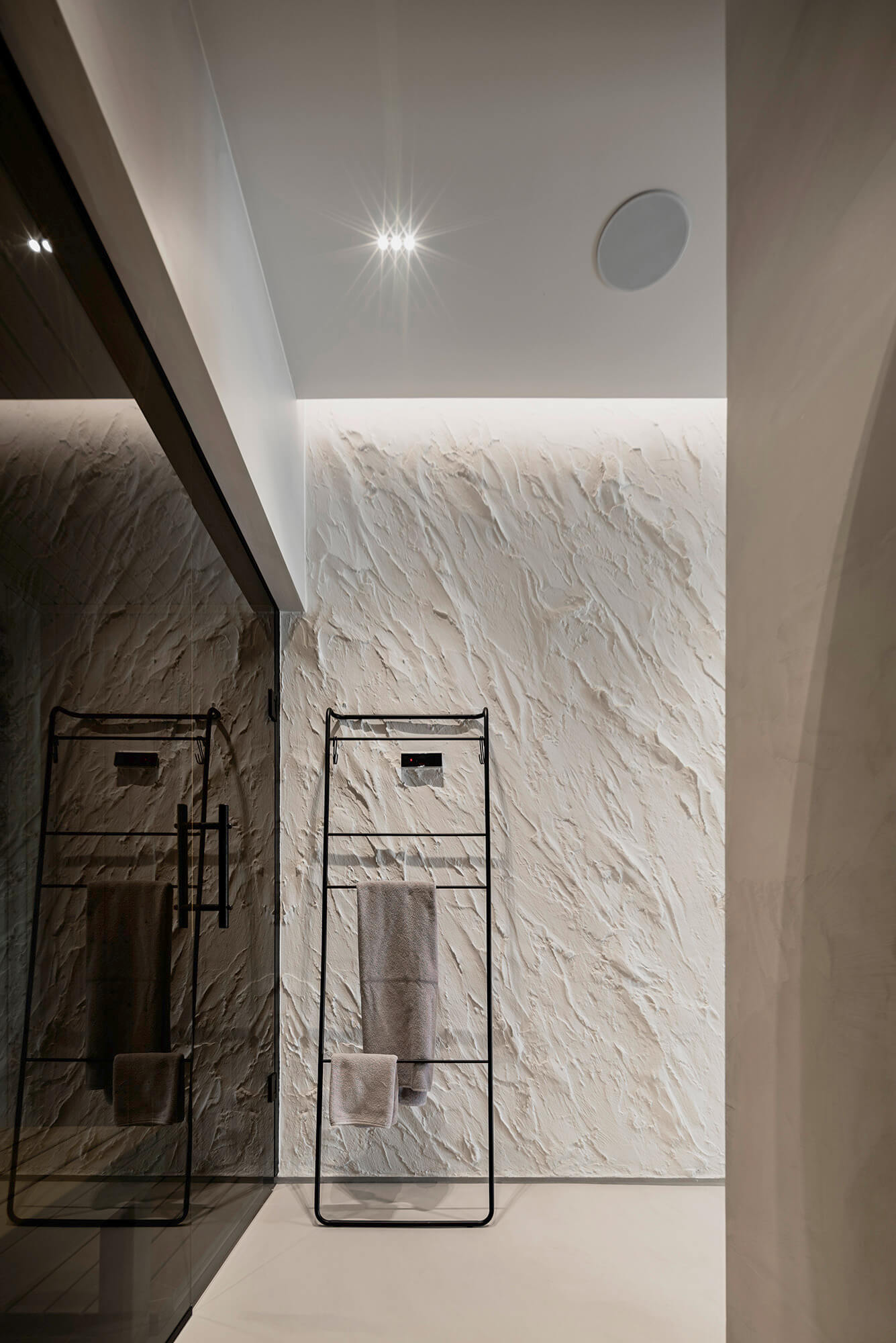 Minimalistyczna łazienka z teksturowaną ścianą i metalowym wieszakiem na ręczniki.