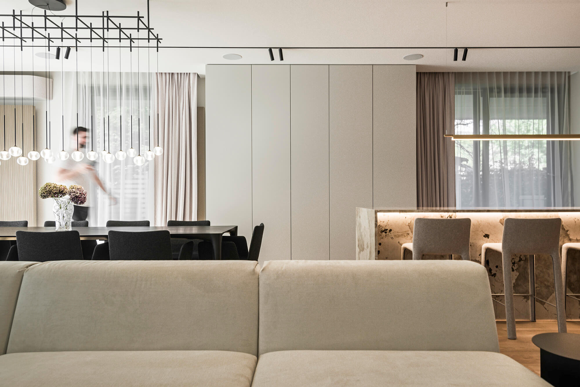 Nowoczesne wnętrze: salon z sofą, jadalnia z krzesłami i barek. Minimalistyczny design, neutralne kolory.