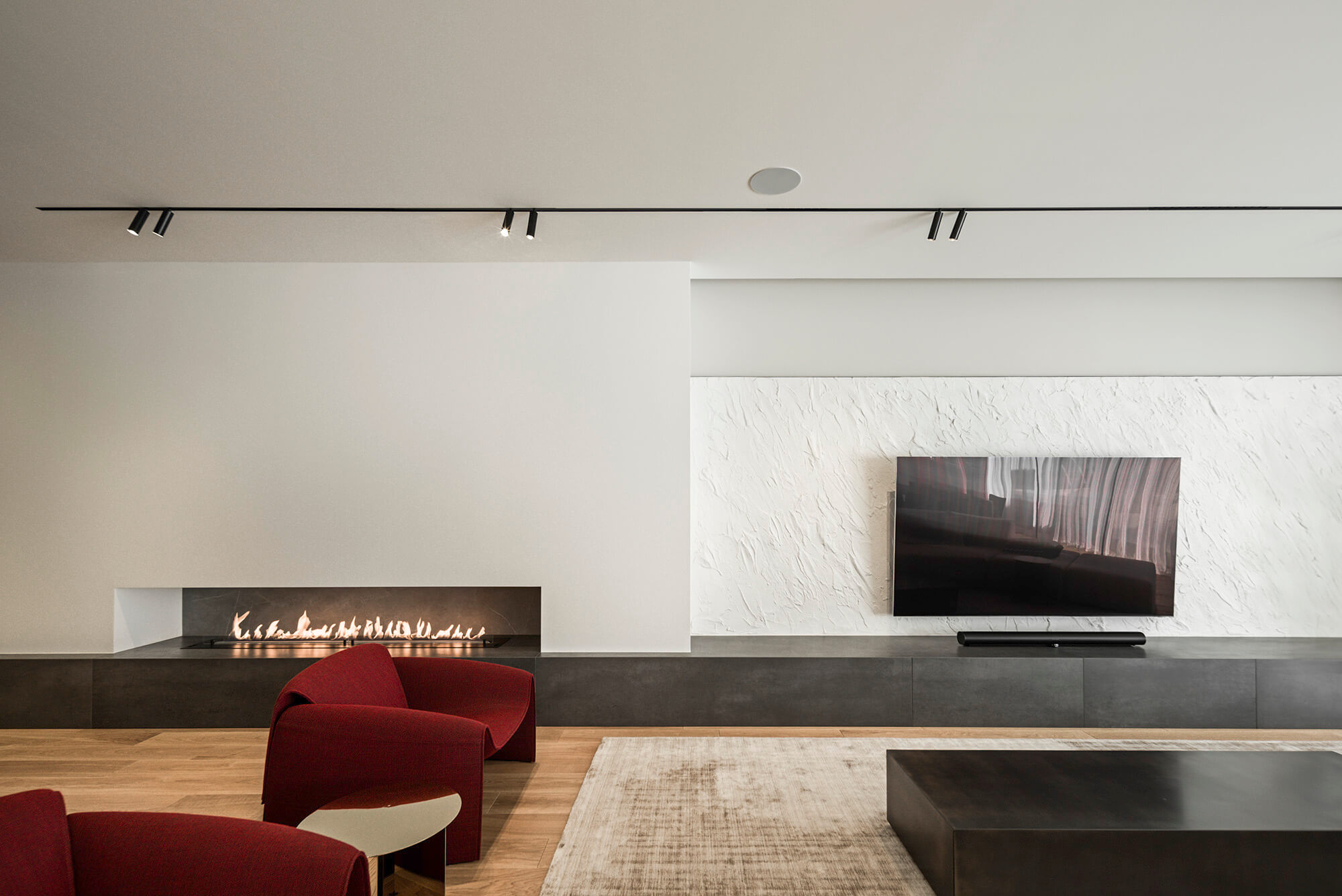 Minimalistyczny salon z kominkiem, czerwonym fotelem i telewizorem na ścianie z teksturą.