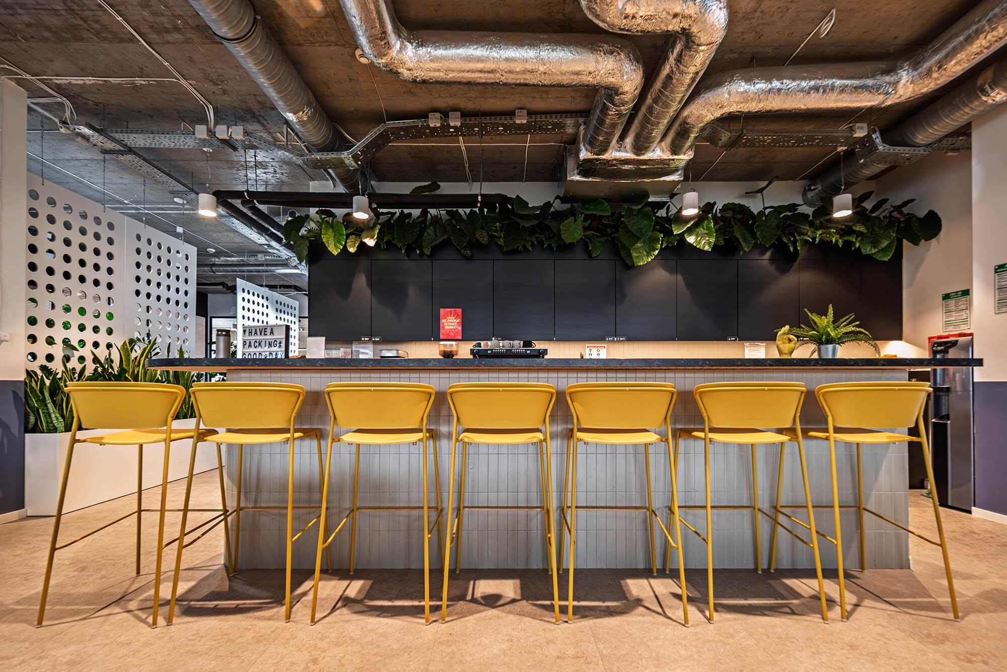 Żółte krzesła barowe przy blacie w nowoczesnym biurze Packhelp. Rośliny dodają świeżości.